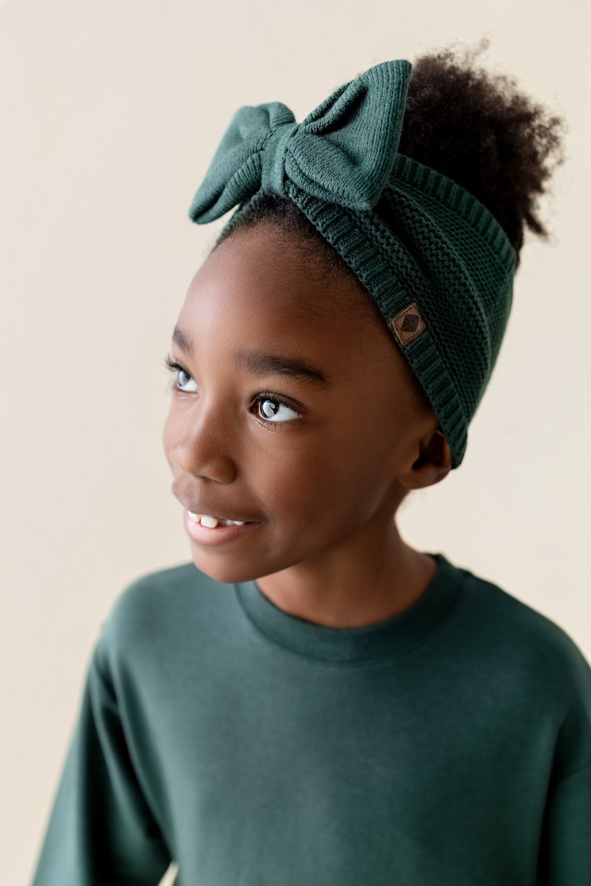 Girl wearing Long Sleeve Skater Dress in Cypress color with Chunky knit knotted bow headband on a beige background