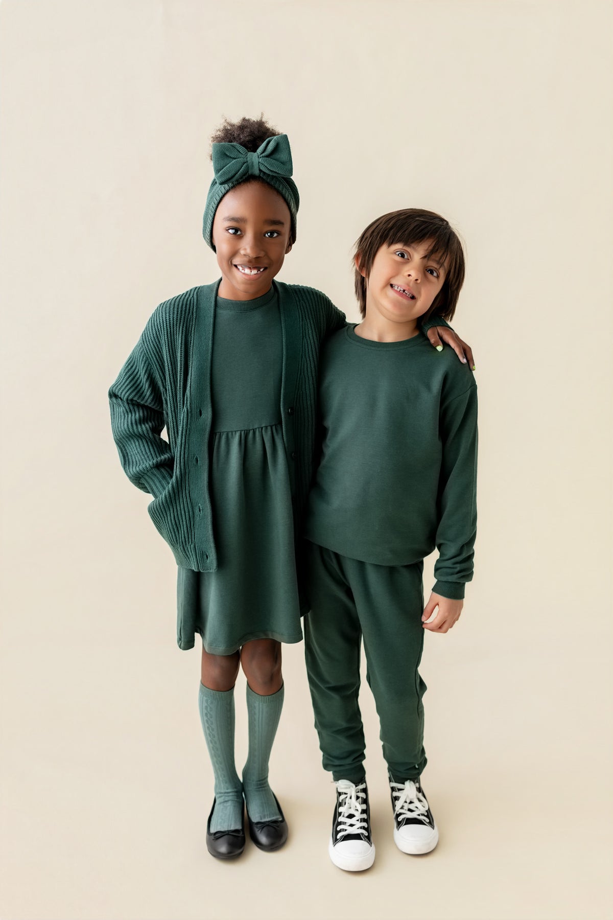 A boy wearing Long Sleeve Jogger Set in Cypress color and girl wearing Long sleeve skater dress in cypress color on a beige background