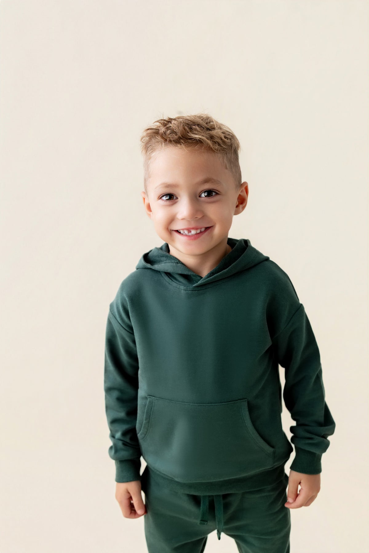 Boy smiling in Hoodie in Cypress color on a beige background