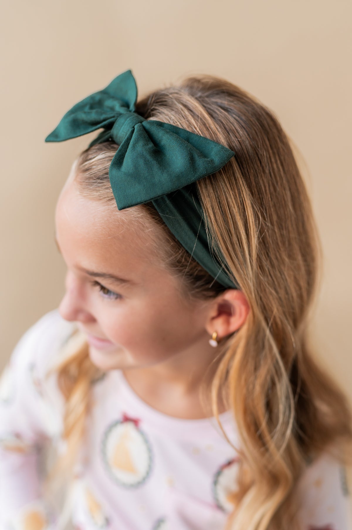 Girl wearing Bow Headband in Cypress color on her head on a beige background