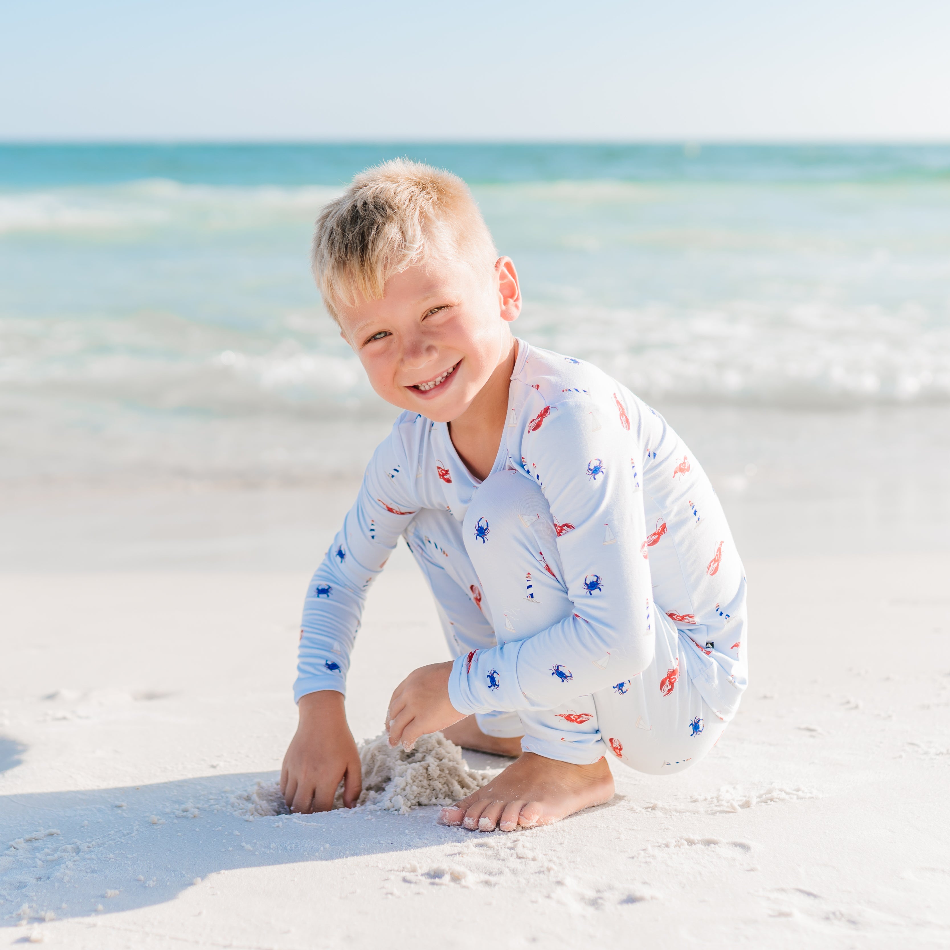 Child Harbor pajamas sitting on a sandy beach with ocean in the background