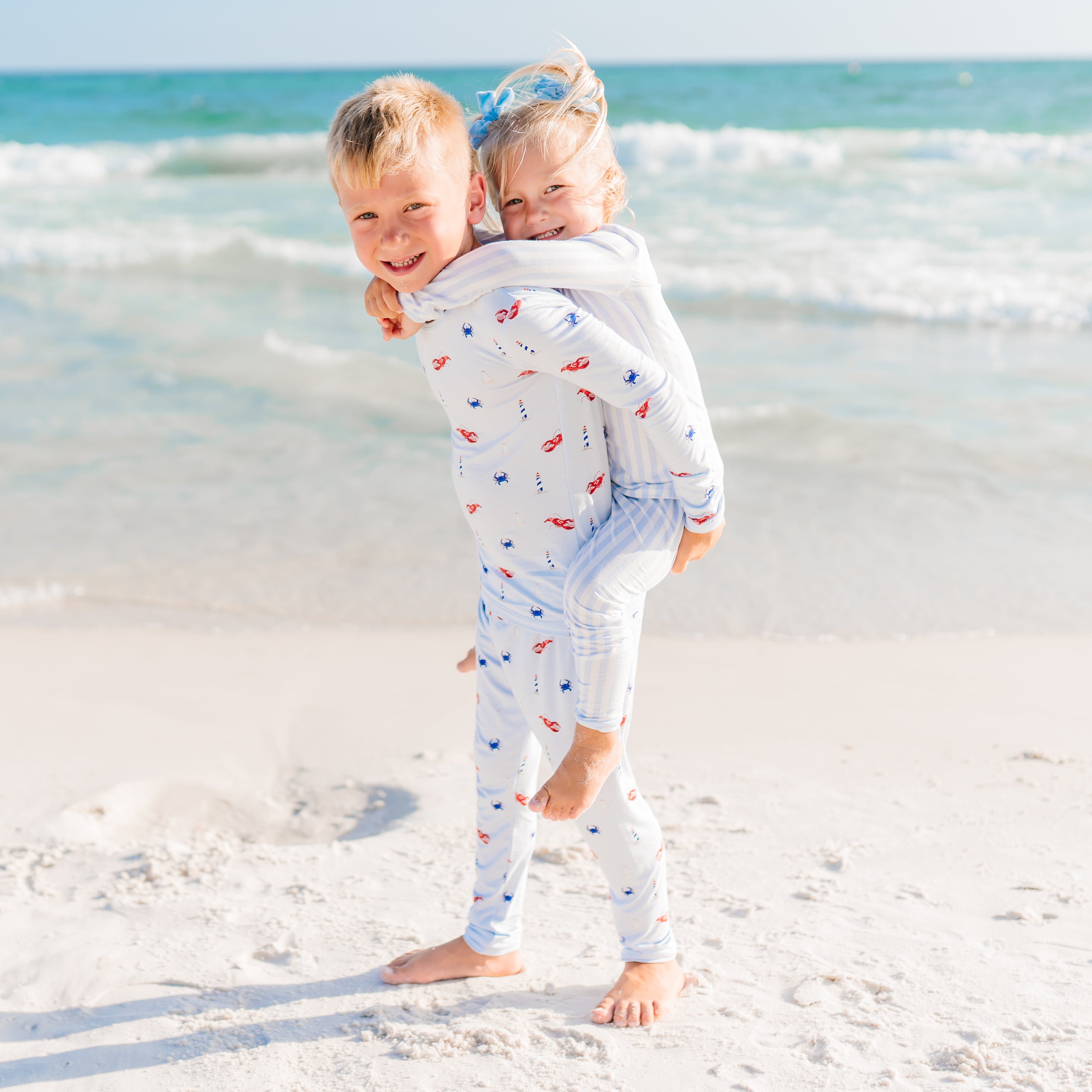 Two children in coordinating pajamas on a beach with ocean in the background