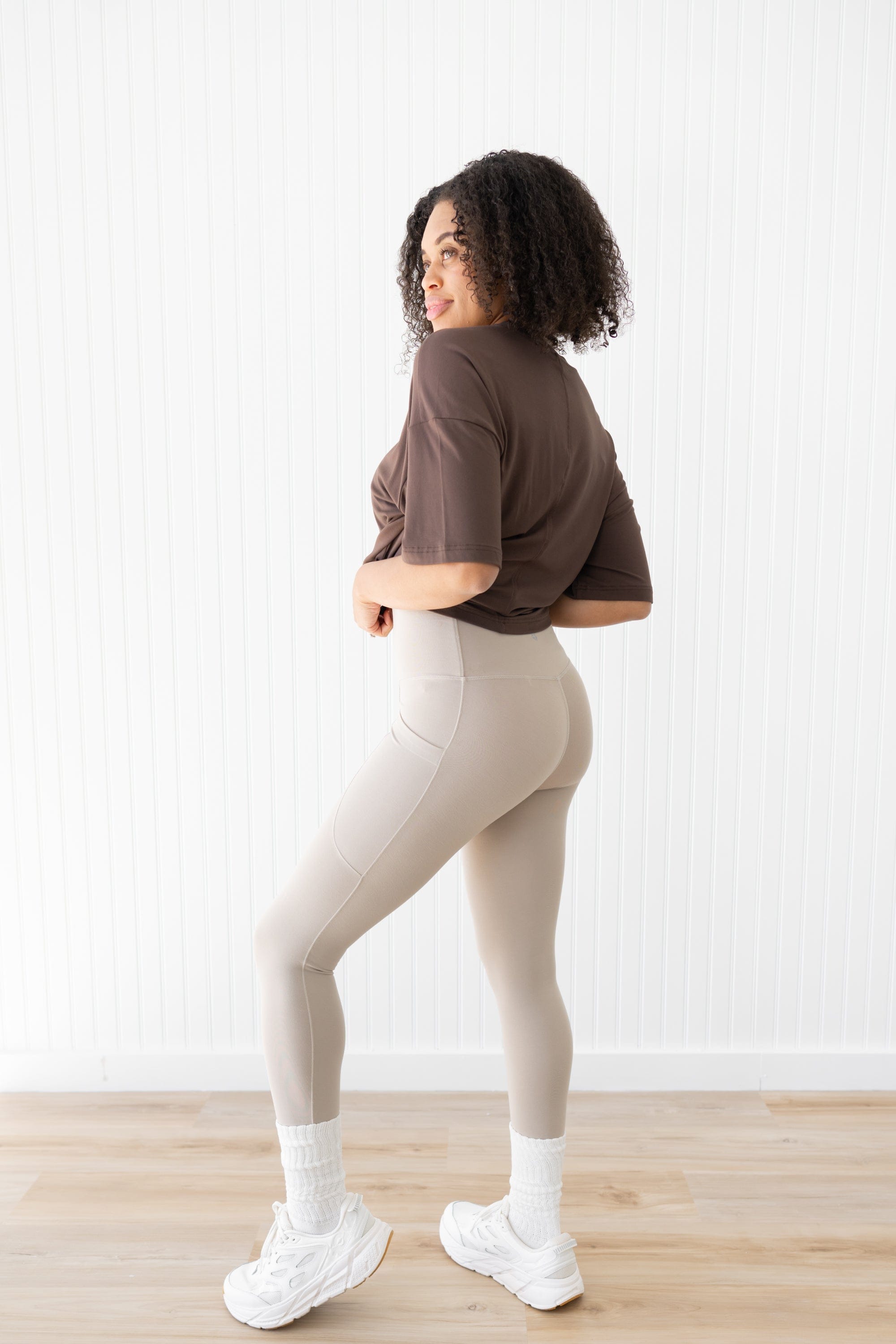 Woman showing the back of bisque leggings and espresso cropped tee with white sneakers