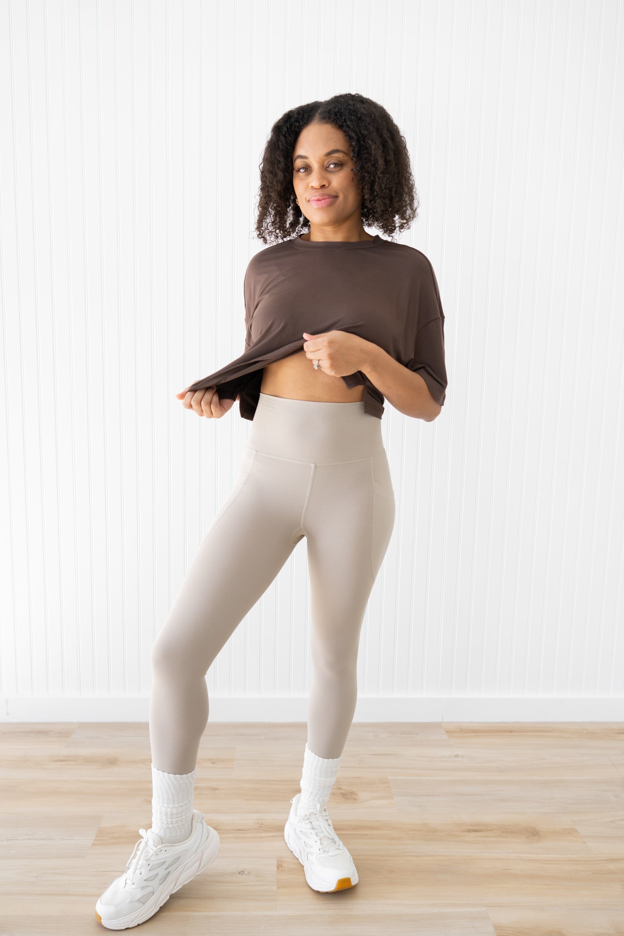 Woman modeling bisque leggings showing waistband and espresso cropped tee with white sneakers