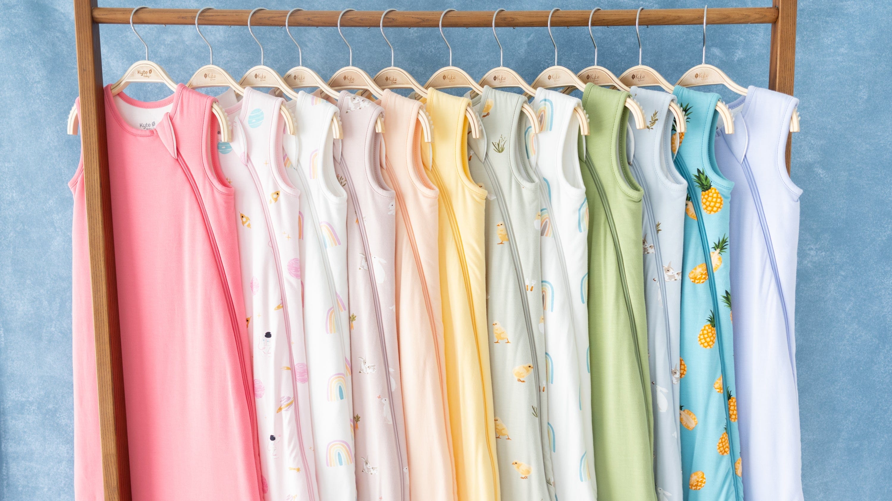 Colorful baby sleep bags on hangers against a blue background