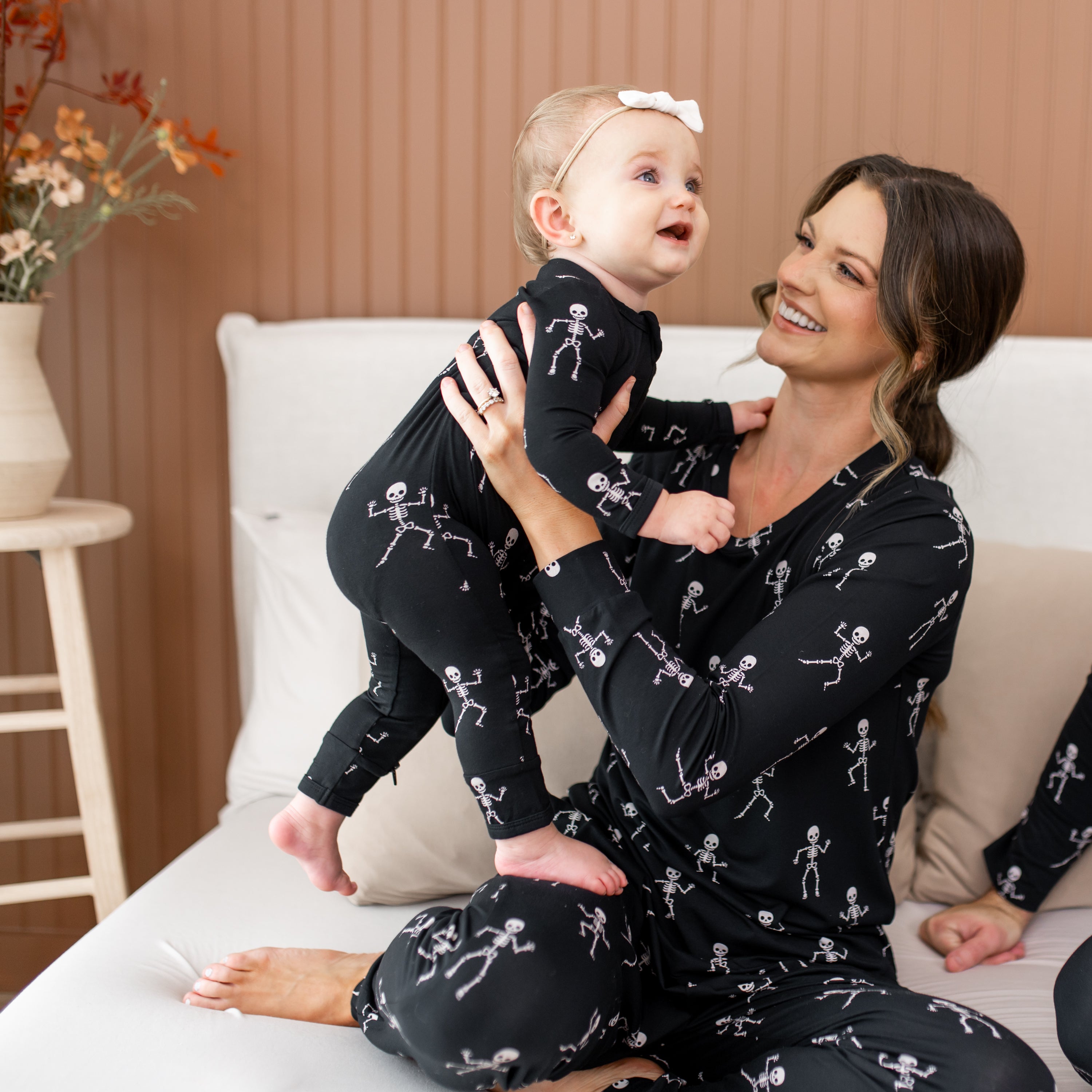 Woman and child wearing matching black pajamas with skeleton patterns on a bed.