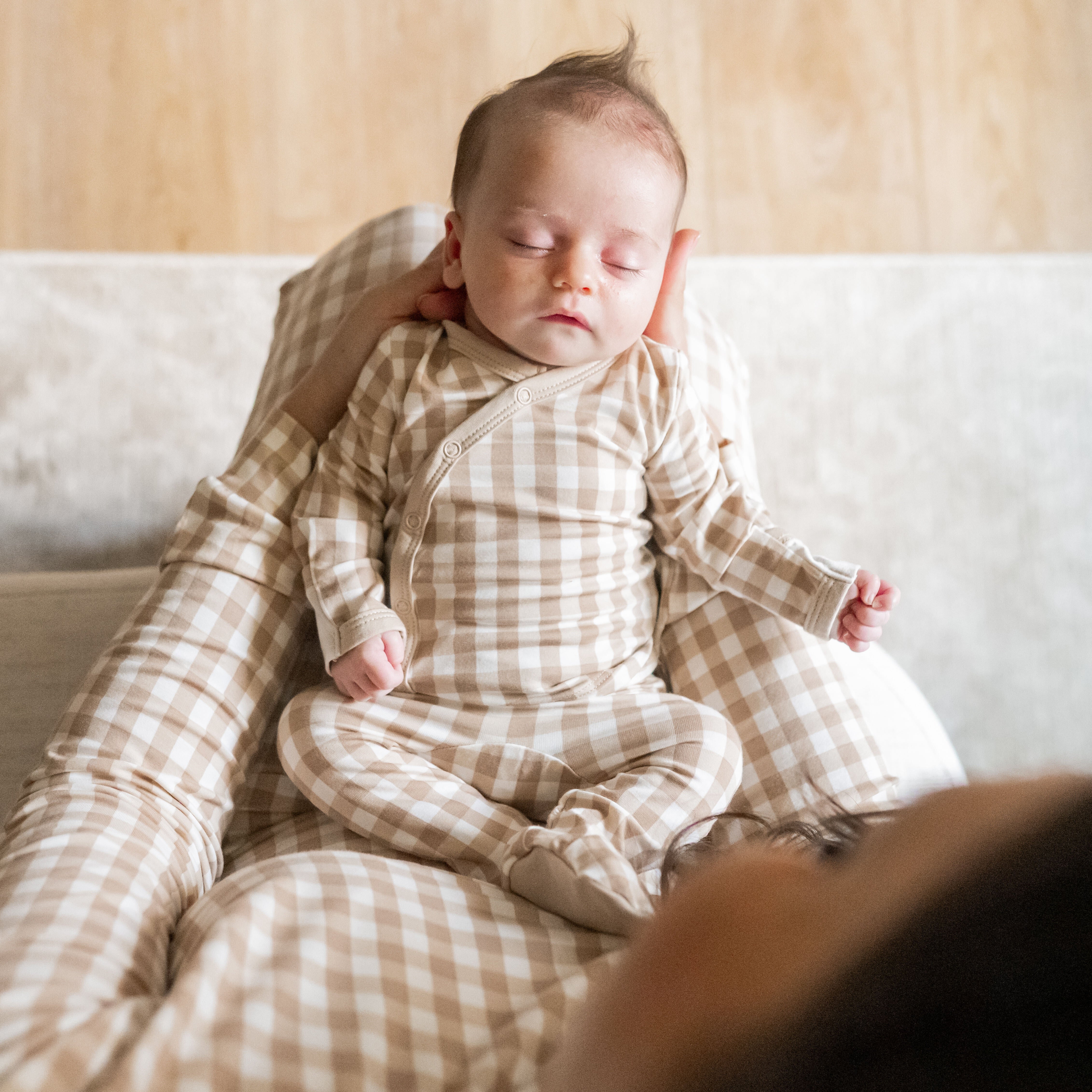 Mother holding newborn wearing the Take Me Home Set with Cap in Gingham Bisque