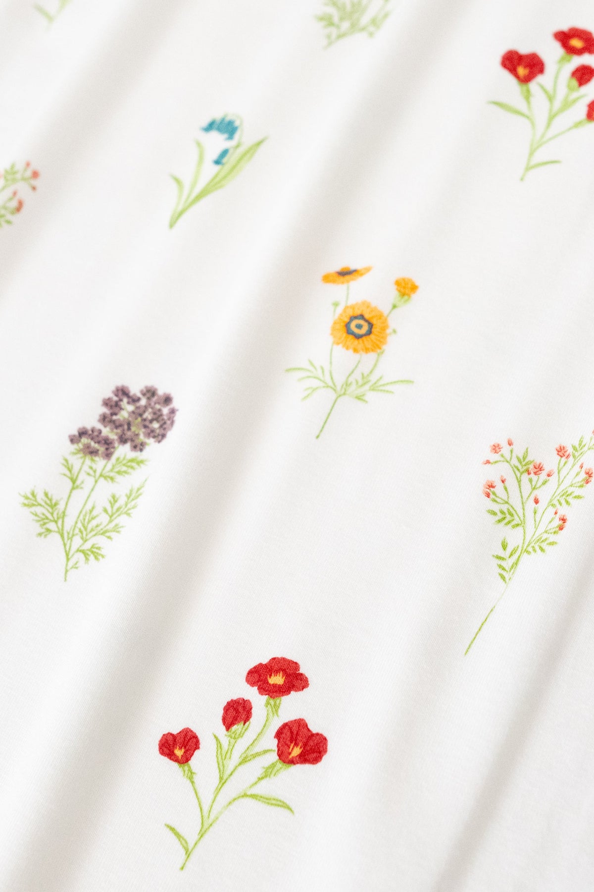 Close up of bamboo fabric: An all-over, repeating print featuring sprigs of light purple Queen Anne’s Lace, dusty blue bluebells, orange globe mallow, yellow coreopsis, and red clarkia over a white background.