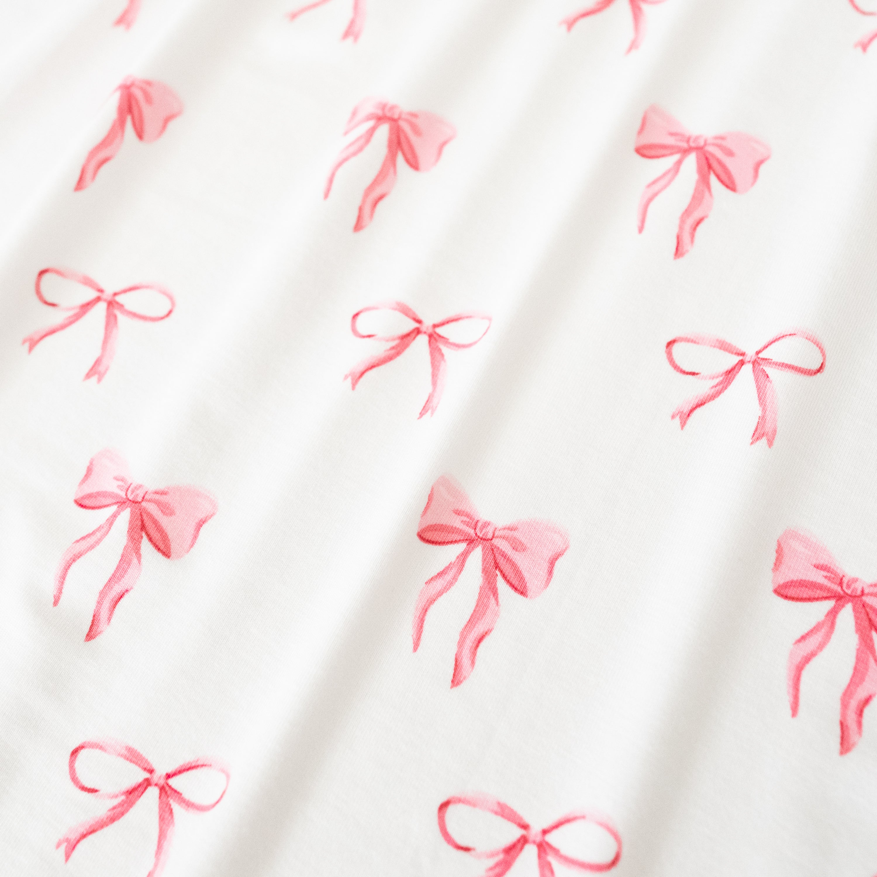 Close up of bamboo fabric: An all-over print of thin and thick light pink bows over a white background.