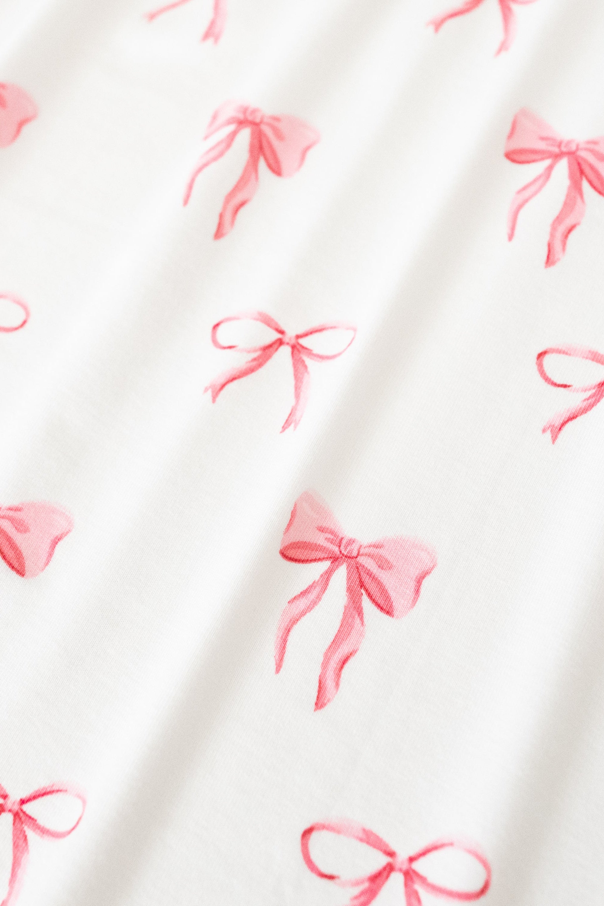 Close up of bamboo fabric: An all-over print of thin and thick light pink bows over a white background.