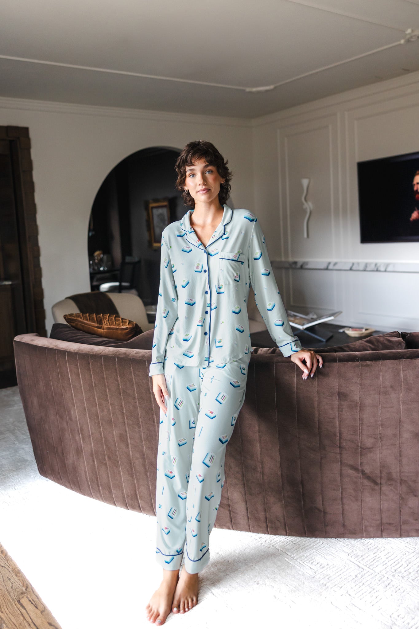 Modal wearing Long-Sleeved Women's Pajama Set in Dew Mahjong print standing against a sofa in a living room