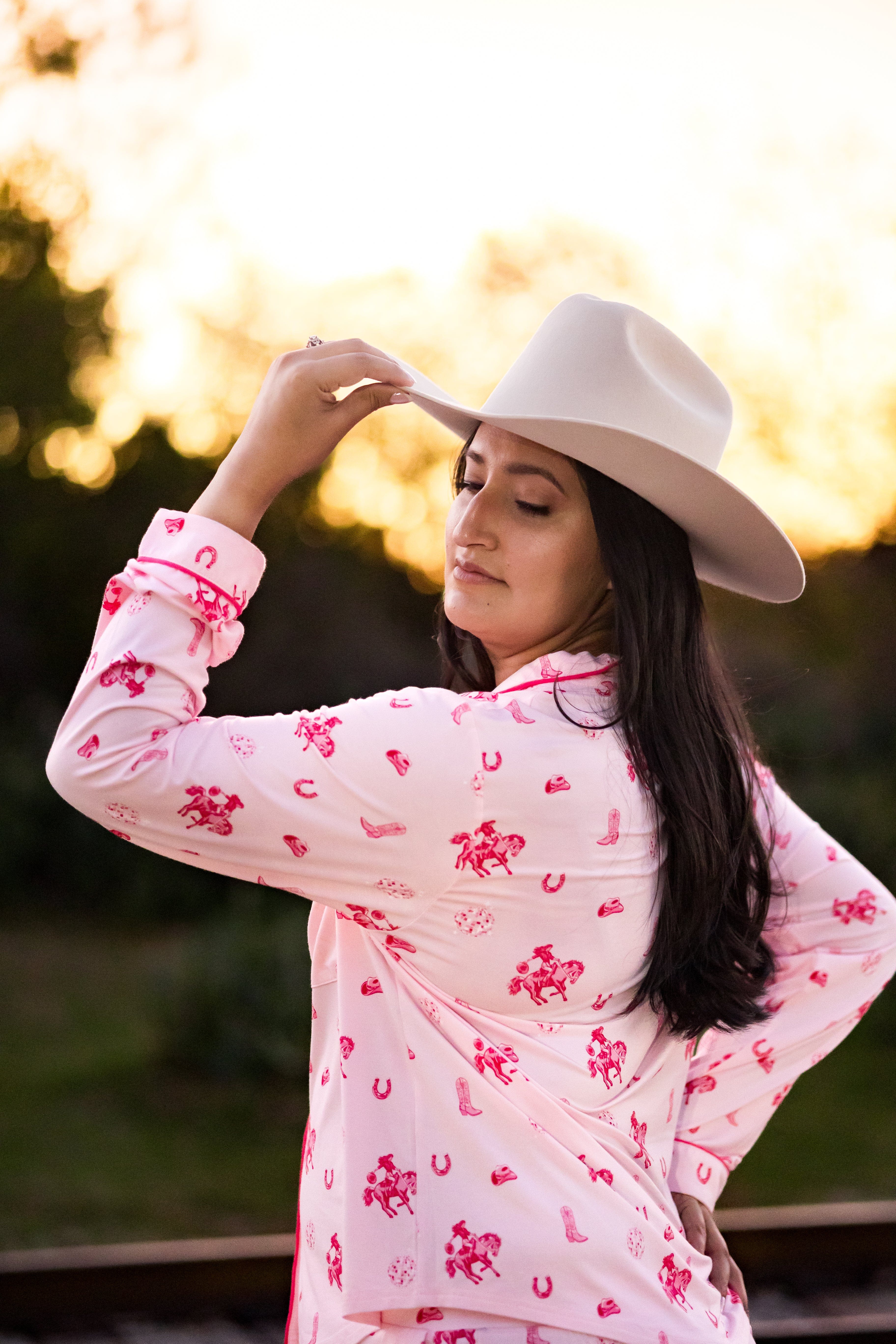 Woman wearing a pink cowgirl pajamas and white cowboy hat with a blurred natural background