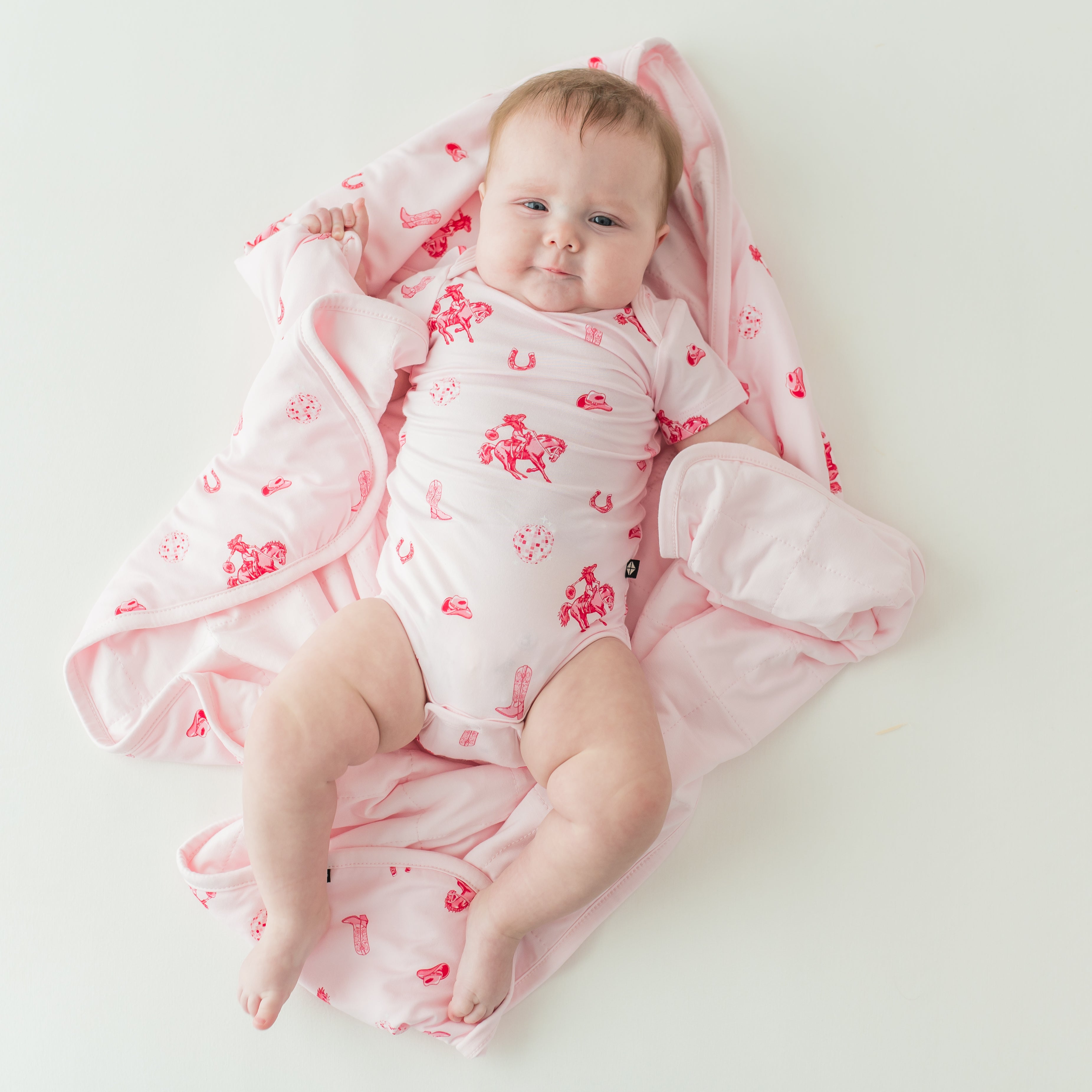 Infant girl wearing the Bodysuit in Disco Cowgirl laying on a matching baby blanket