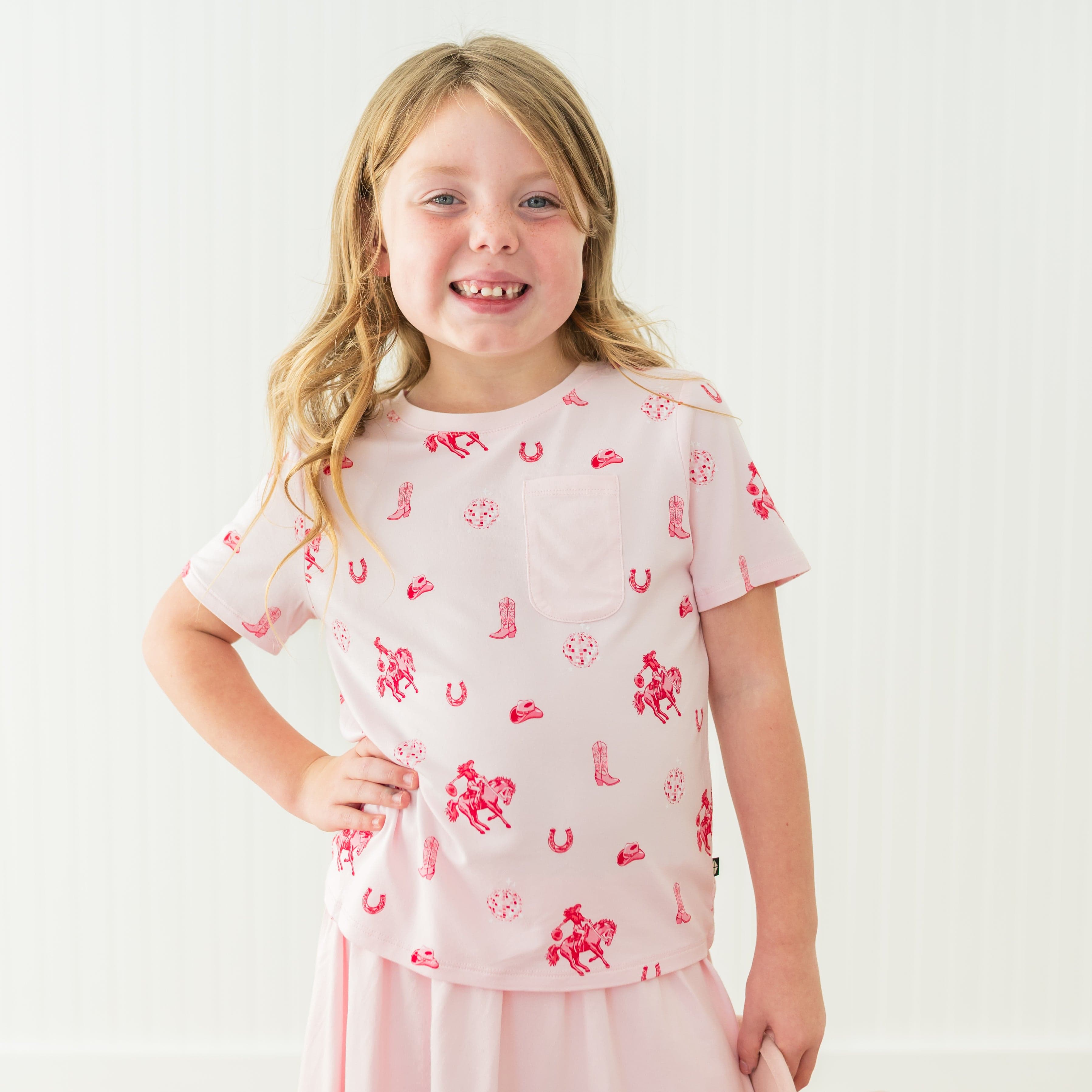 Smiling girl standing with one hand on her hip wearing the Toddler Crew Neck Tee in Disco Cowgirl