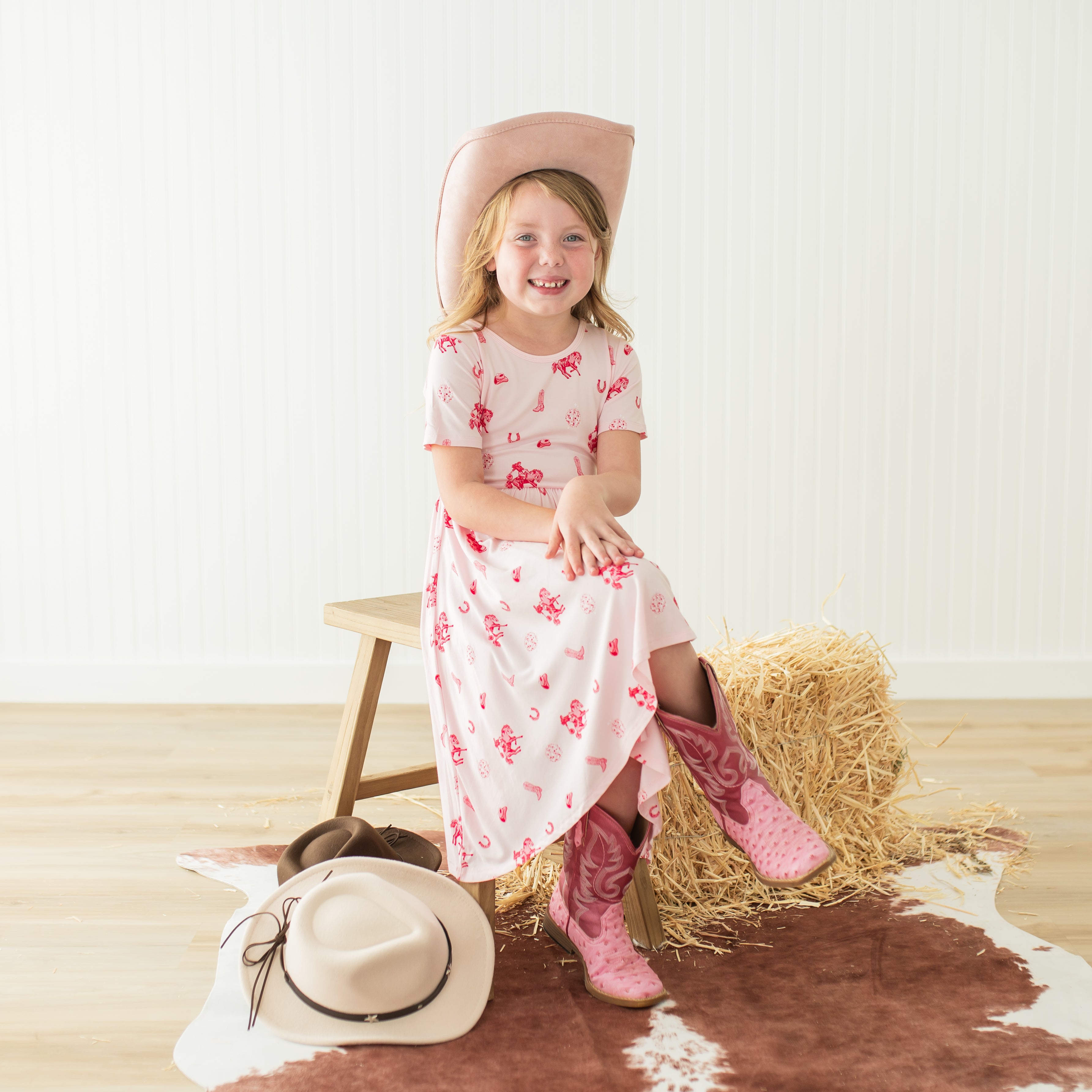 Young smiling girl sitting posing on a wooden bench wearing the Twirl Dress in Disco Cowgirl