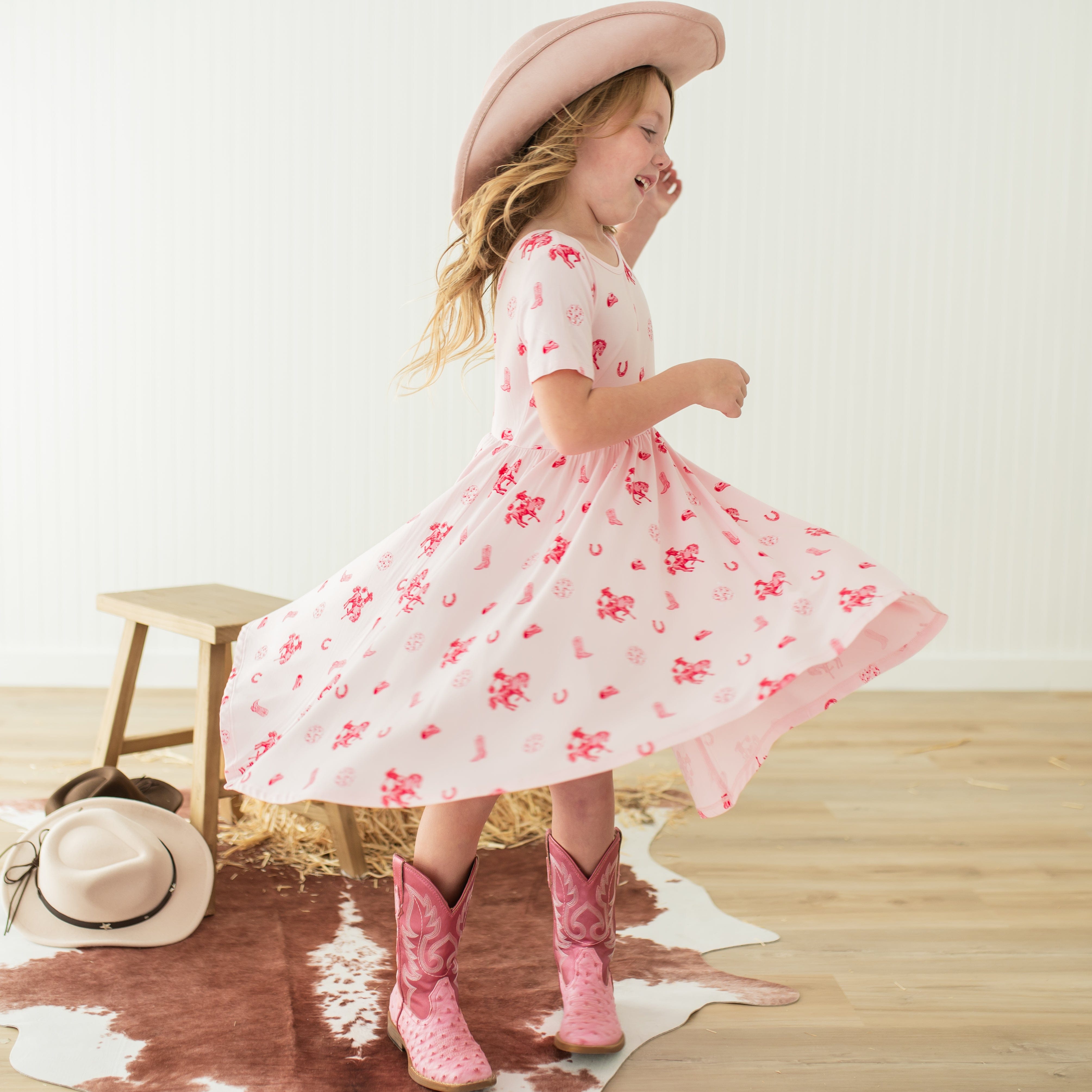Young girl twirling wearing the Twirl Dress in Disco Cowgirl with a pink cowboy hat on