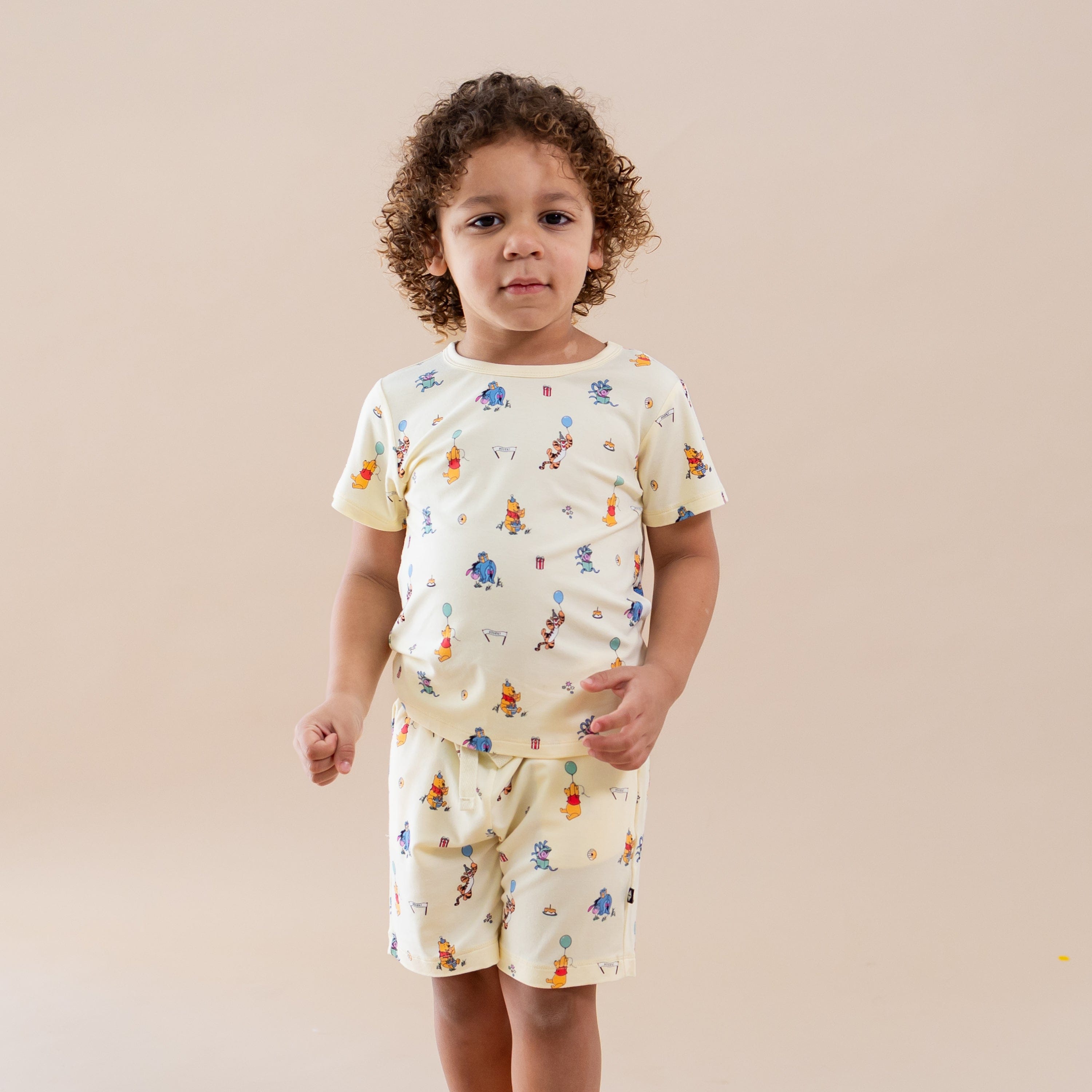 Young boy wearing the Drawstring Short in Winnie the Pooh Celebration paired with a matching basic tee