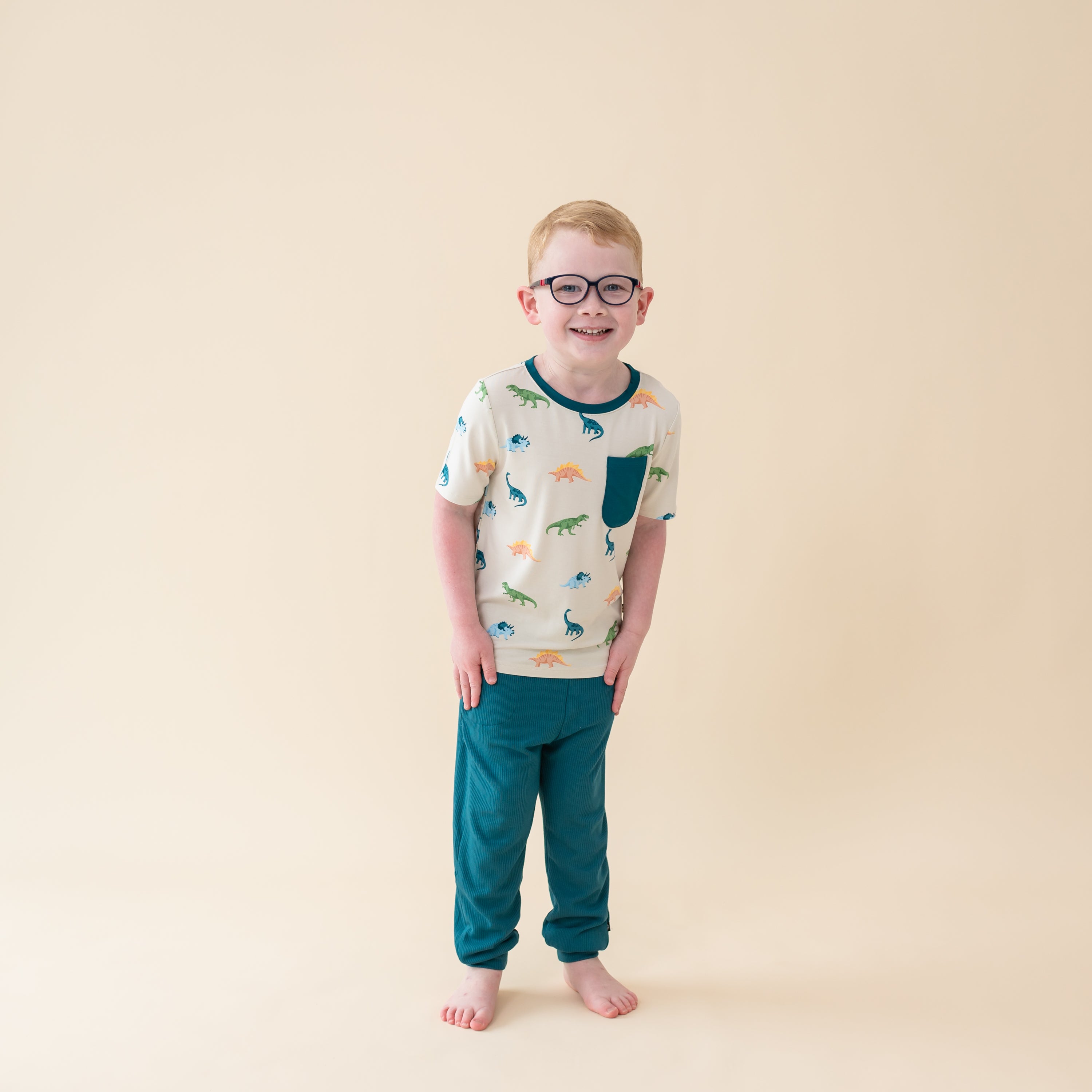 Young boy in Ecru Roar Short Sleeve Toddler Crew Neck Tee. The shirt has a pocket accent in the color Loch and is paire with Loch pants
