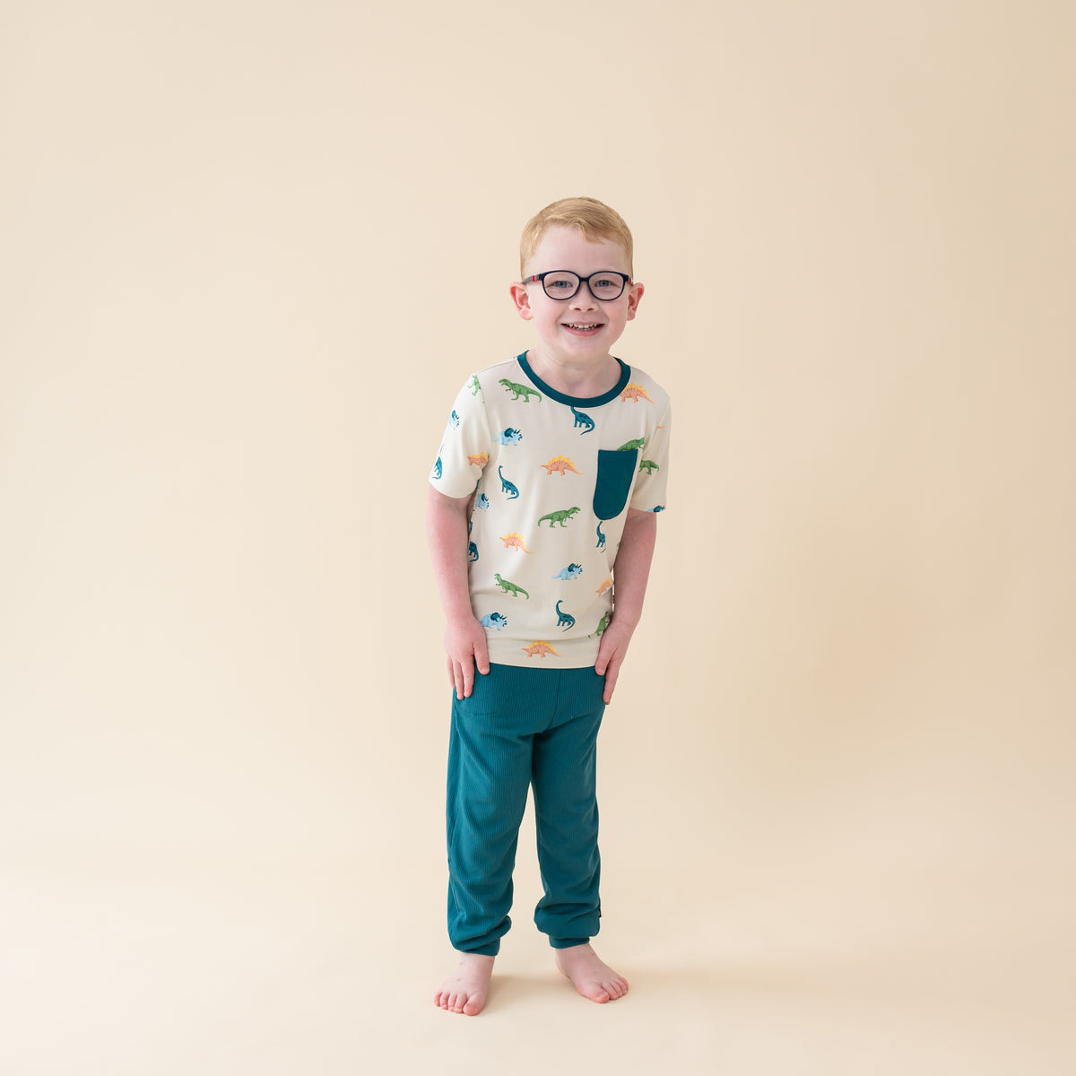 Young boy in Ecru Roar Short Sleeve Toddler Crew Neck Tee. The shirt has a pocket accent in the color Loch and is paire with Loch pants
