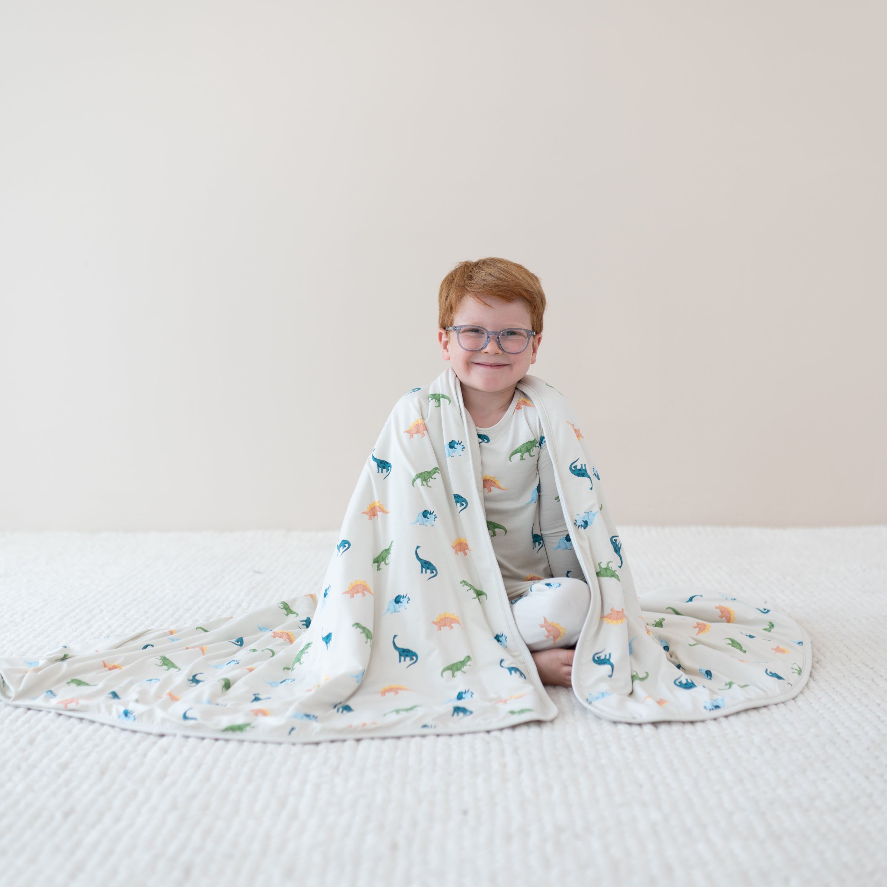 Child sitting and wearing in Ecru Roar Pajamas while wrapped in Youth Blanket in Ecru Roar 1.0
