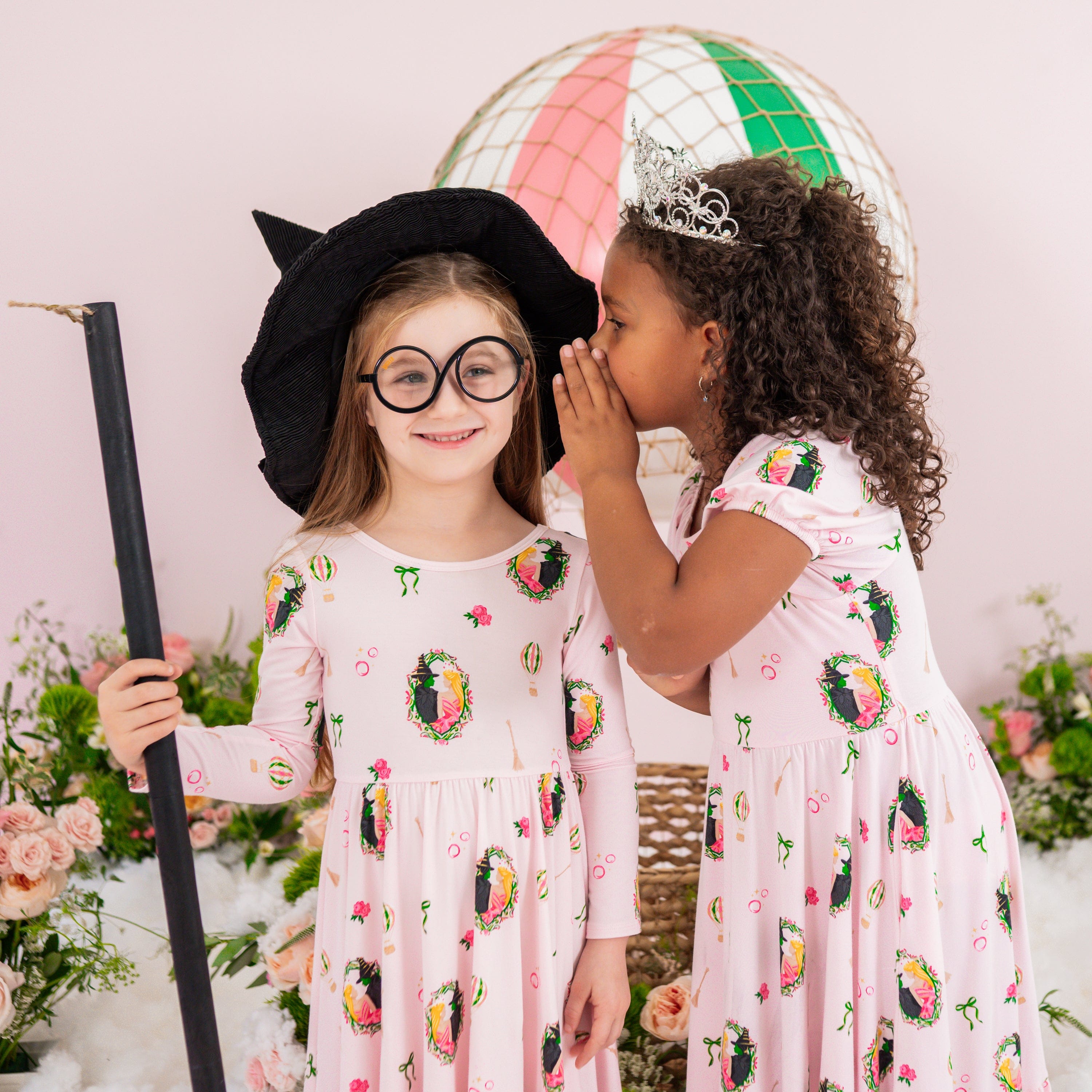 Two young girls standing side by side wearing the long sleeve and puff sleeve twirl dresses in front of a hot air balloon floral backdrop