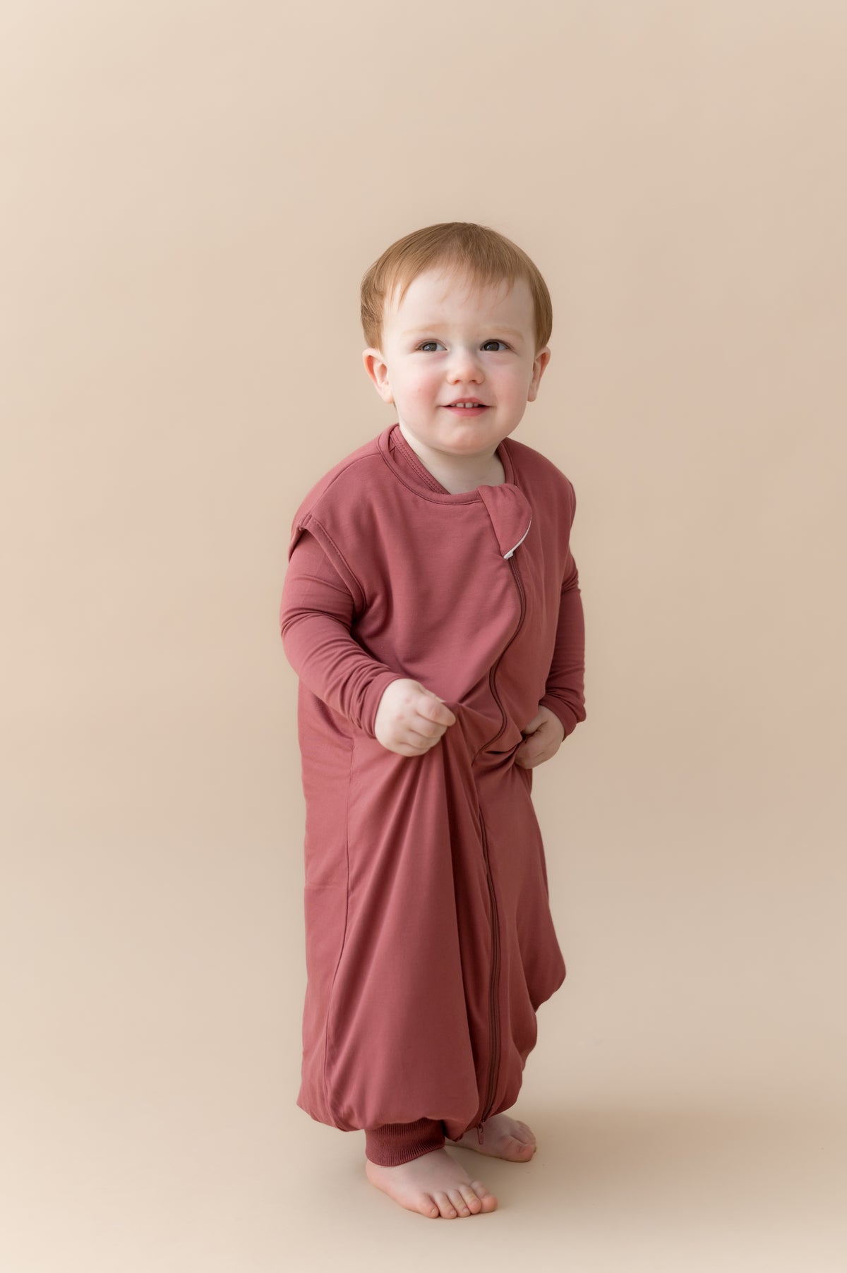 Child standing wearing Sleep Bag Walker in Ember 1.0 on a beige background