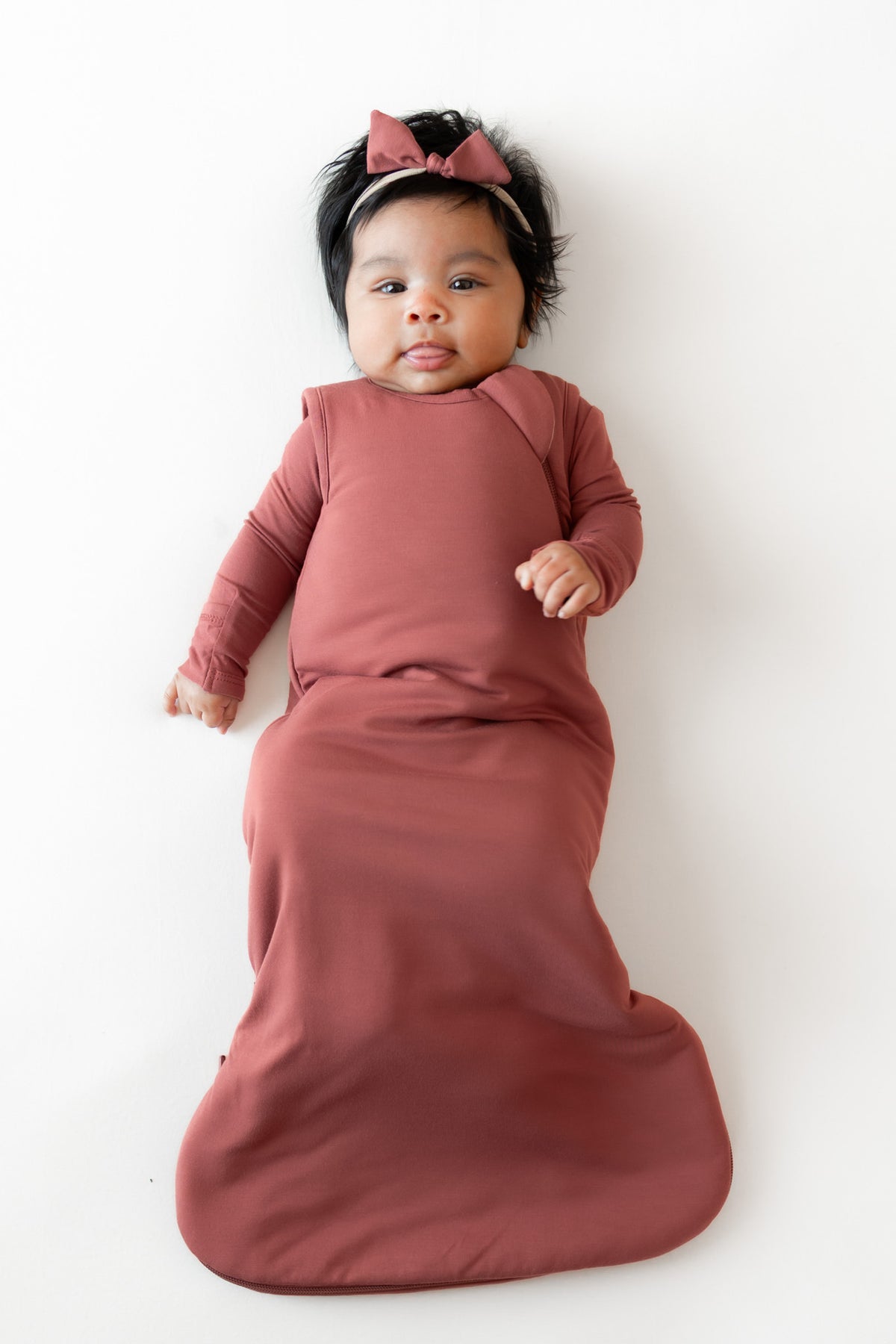 Baby wearing Tiny Nylon Bow in Ember with sleep bag in ember on a white background