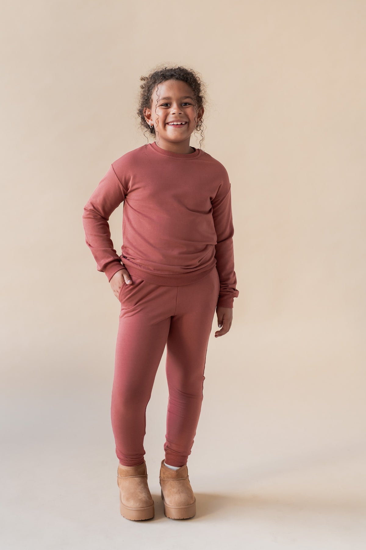 Girl smiling in Jogger Pant in Ember color under similar color sweatshirt on a beige background