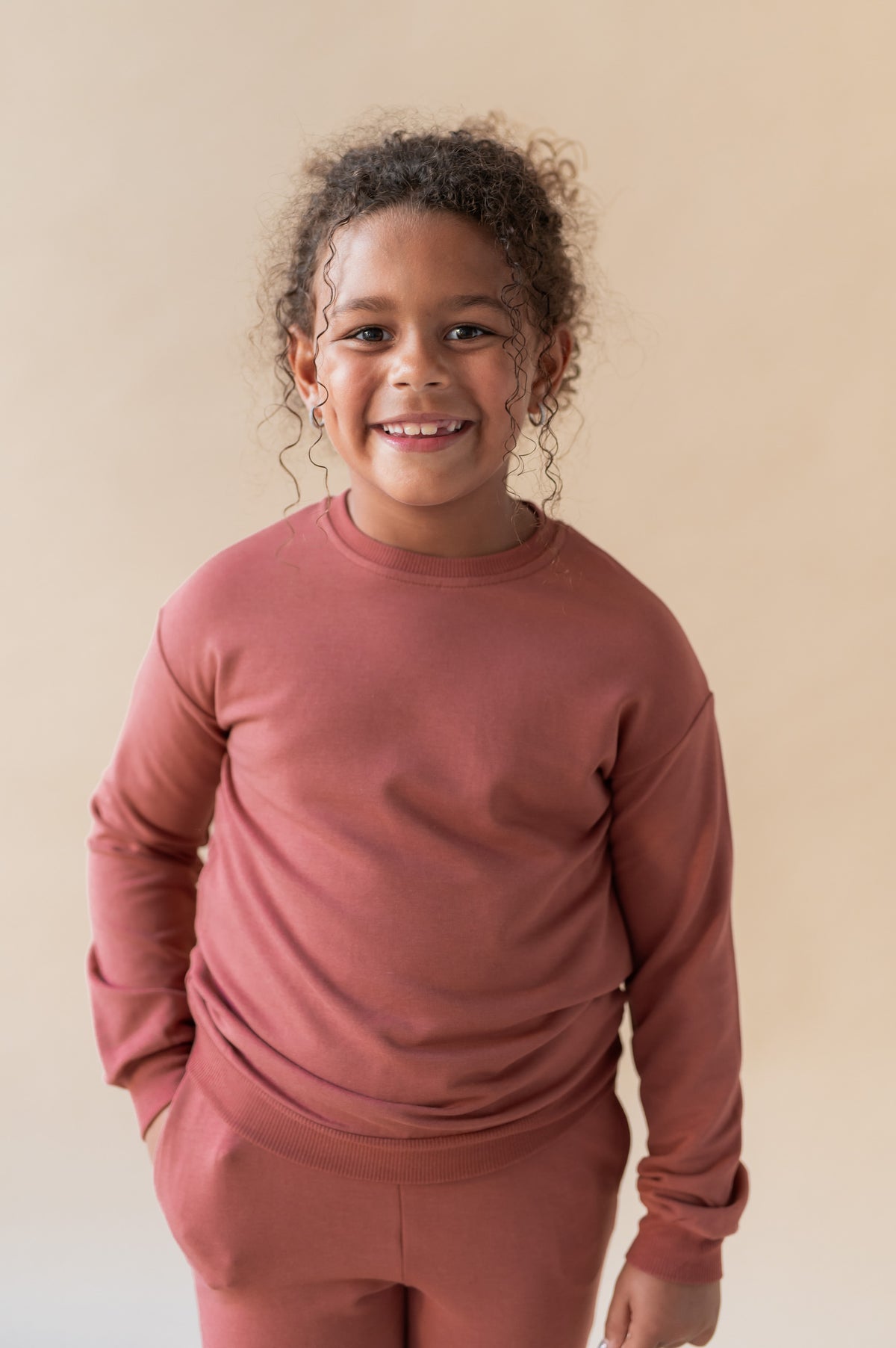 Girl wearing Sweatshirt in Cypress color over similar color jogger pant on a beige background