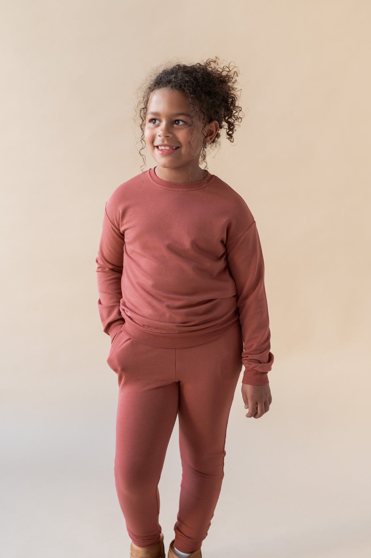 Girl posing in Jogger Pant in Ember color under similar color sweatshirt on a beige background