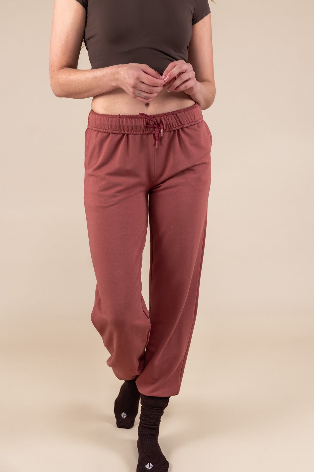 Modal wearing Women's Jogger Pant in Ember color under a brown shirt on a beige background