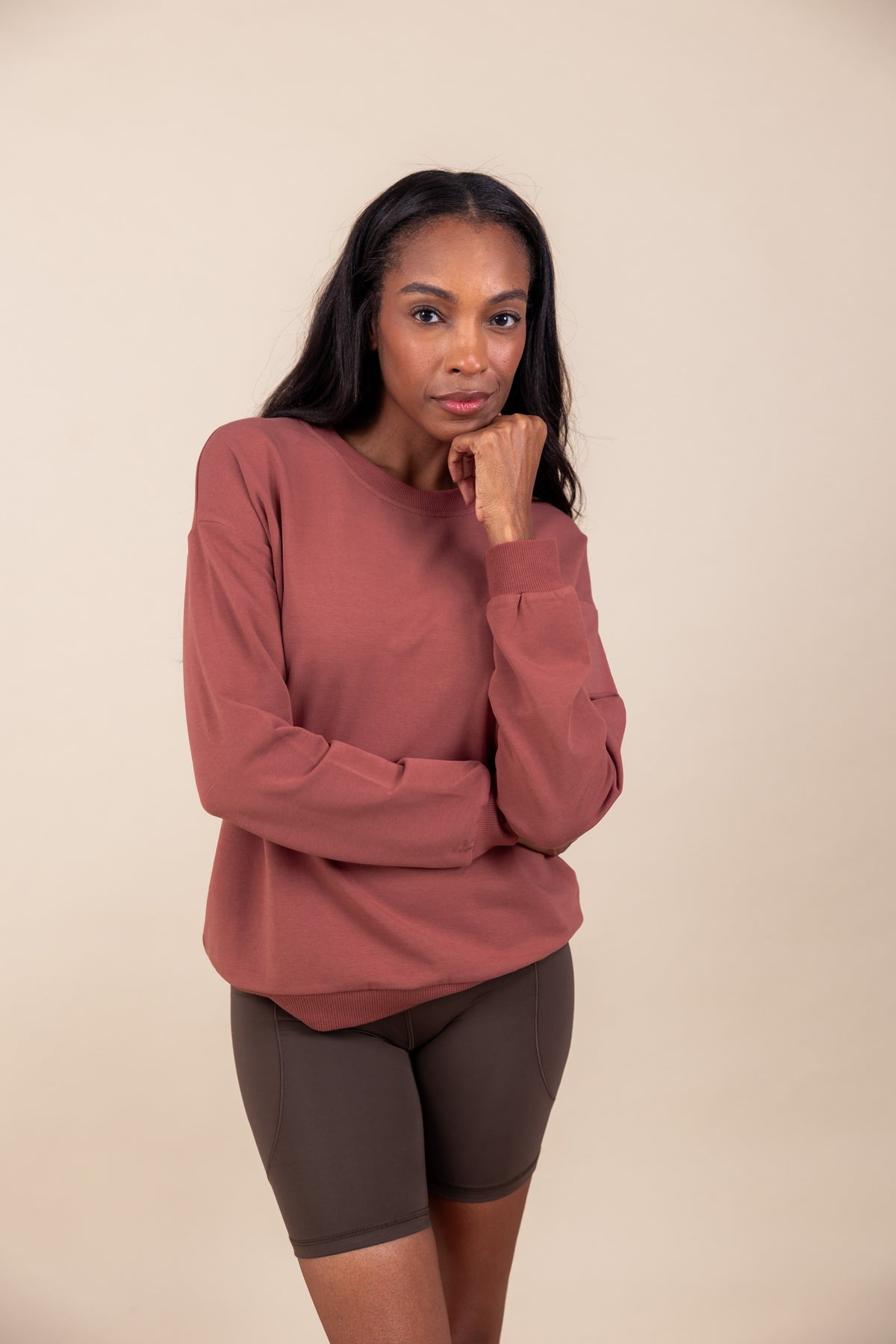Woman wearing Women's Sweatshirt in Ember color over brown shorts on a beige background