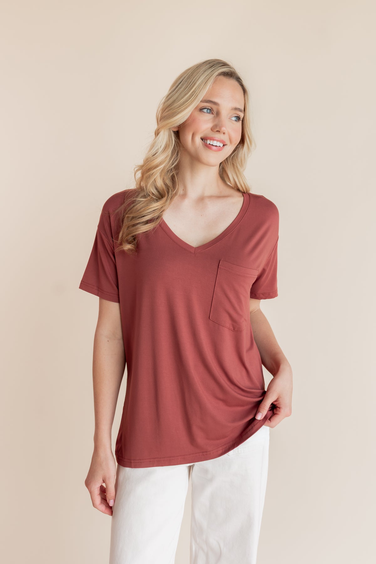 Model posing in Women's Oversized V-Neck Tee in Ember over white pants on a beige background