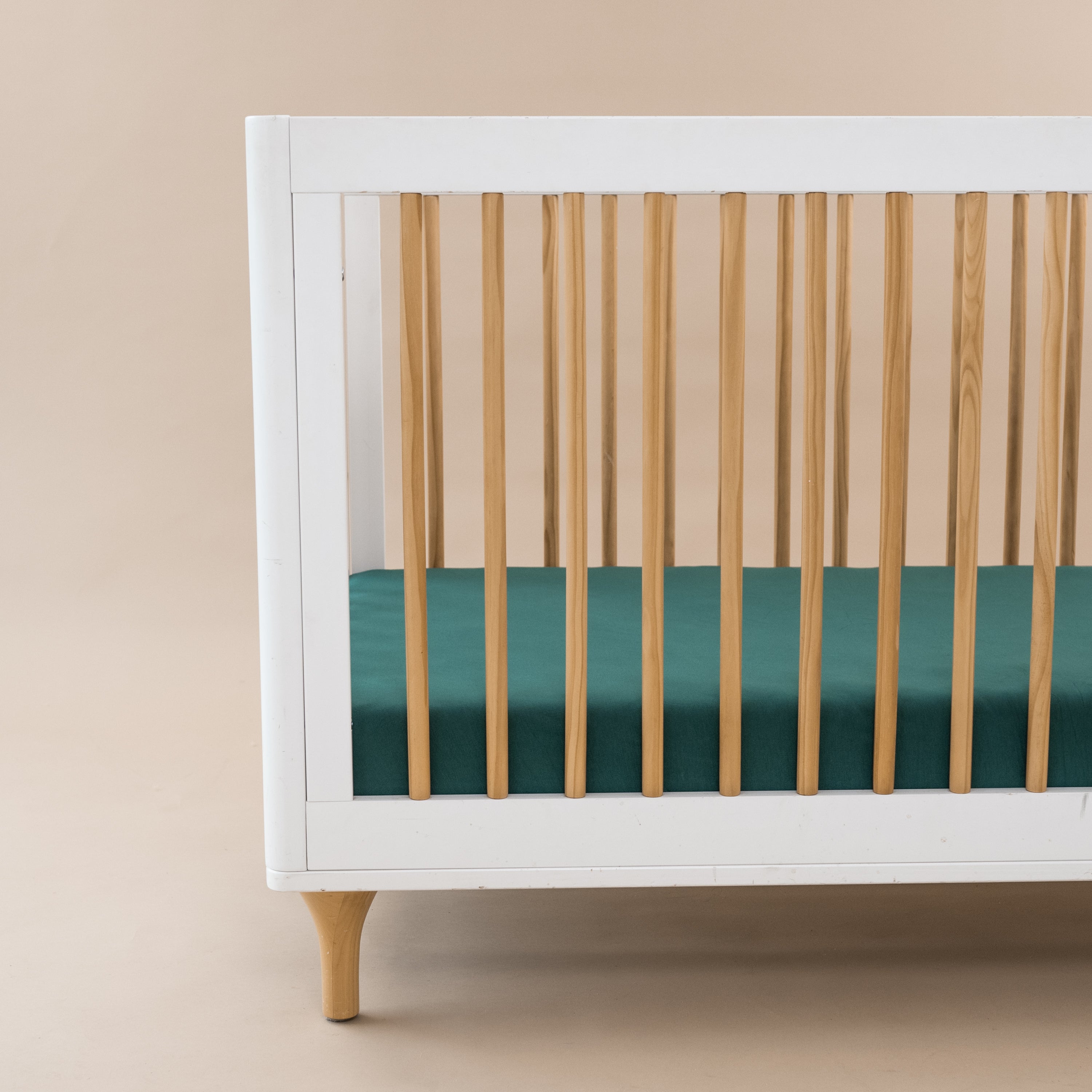 Crib Sheet in Emerald shown on a mattress in a modern white and wooden crib
