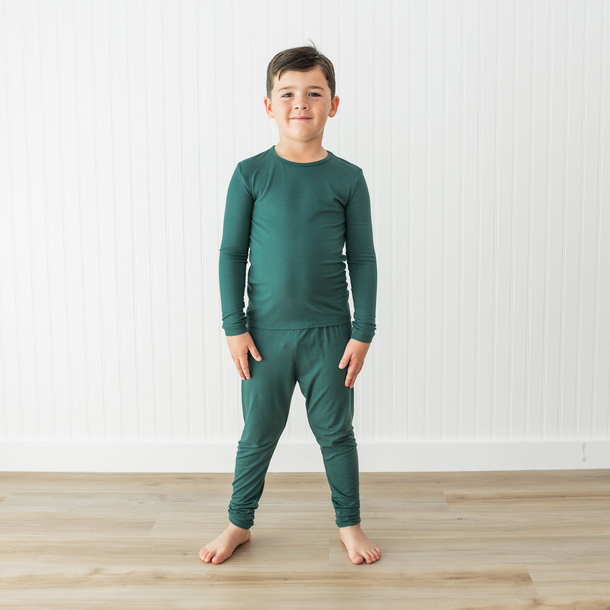 Child wearing a green pajama set standing on a wooden floor with a white background