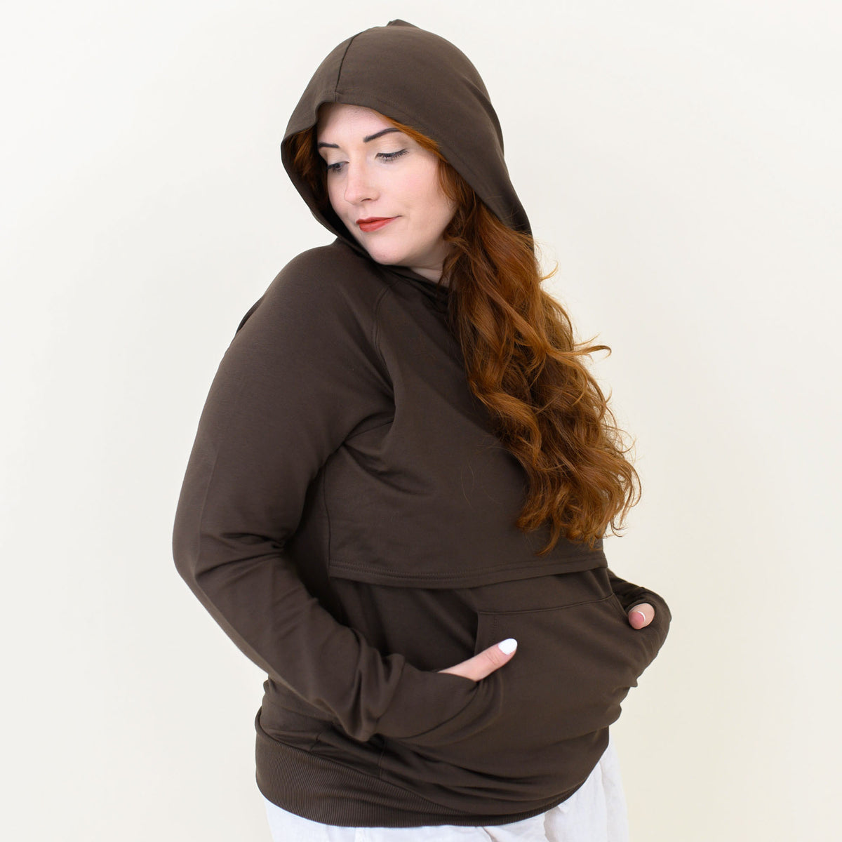 Smiling female wearing the Women's French Terry Nursing Hoodie in Espresso with the hood up and her hands in the kangaroo pocket