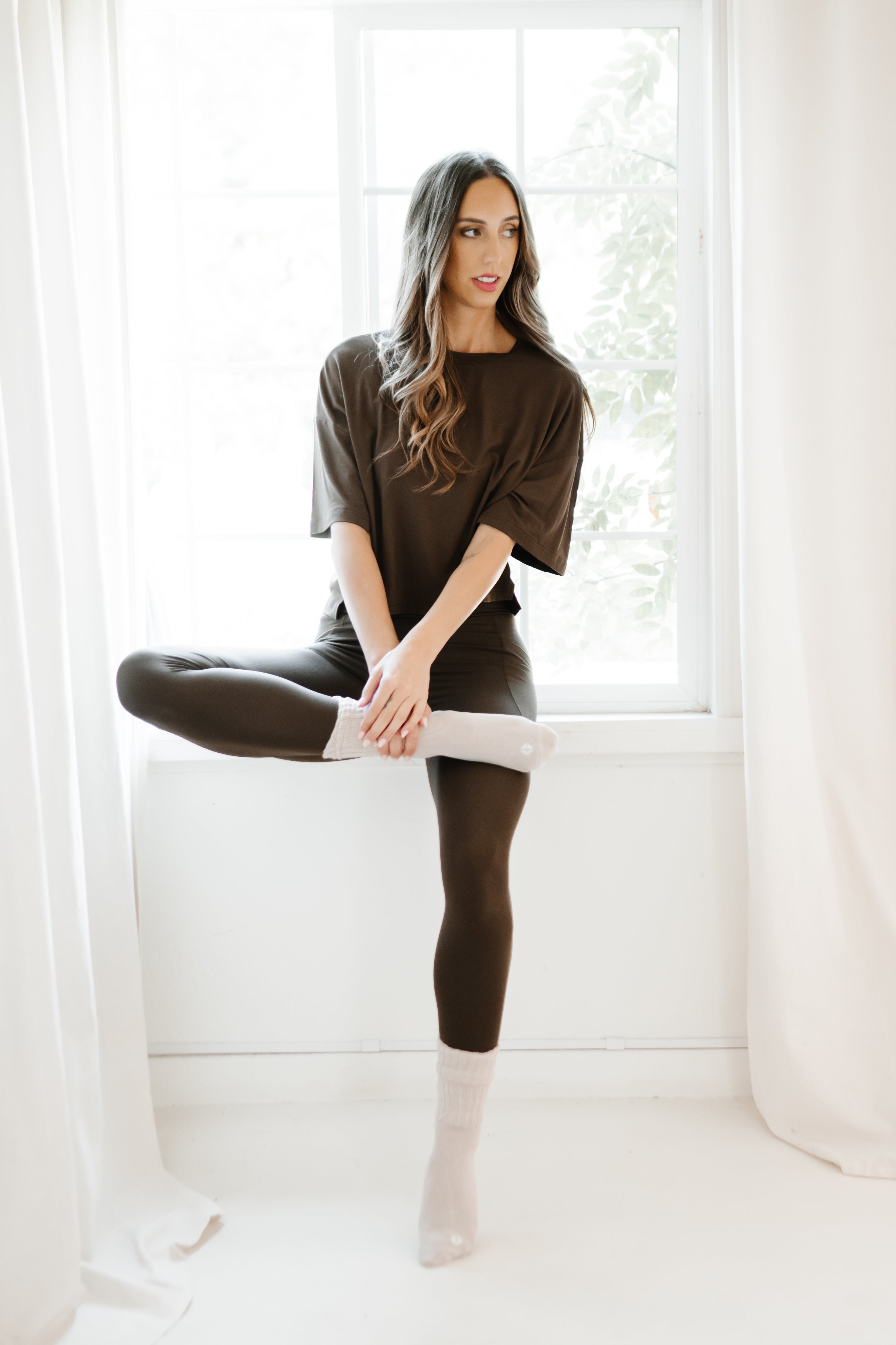 Female model sitting on a window sill wearing the Bamboo Flex Women’s Leggings in Espresso and short sleeve tee