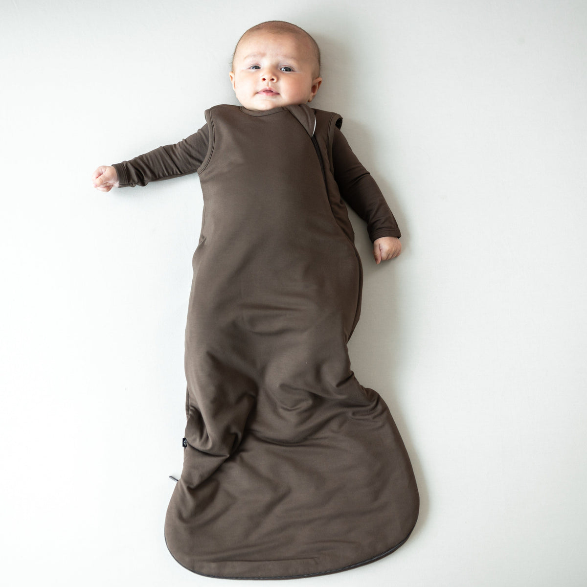 Infant laying down wearing the Sleep Bag in Espresso 1.0 with a matching long sleeve romper on underneath