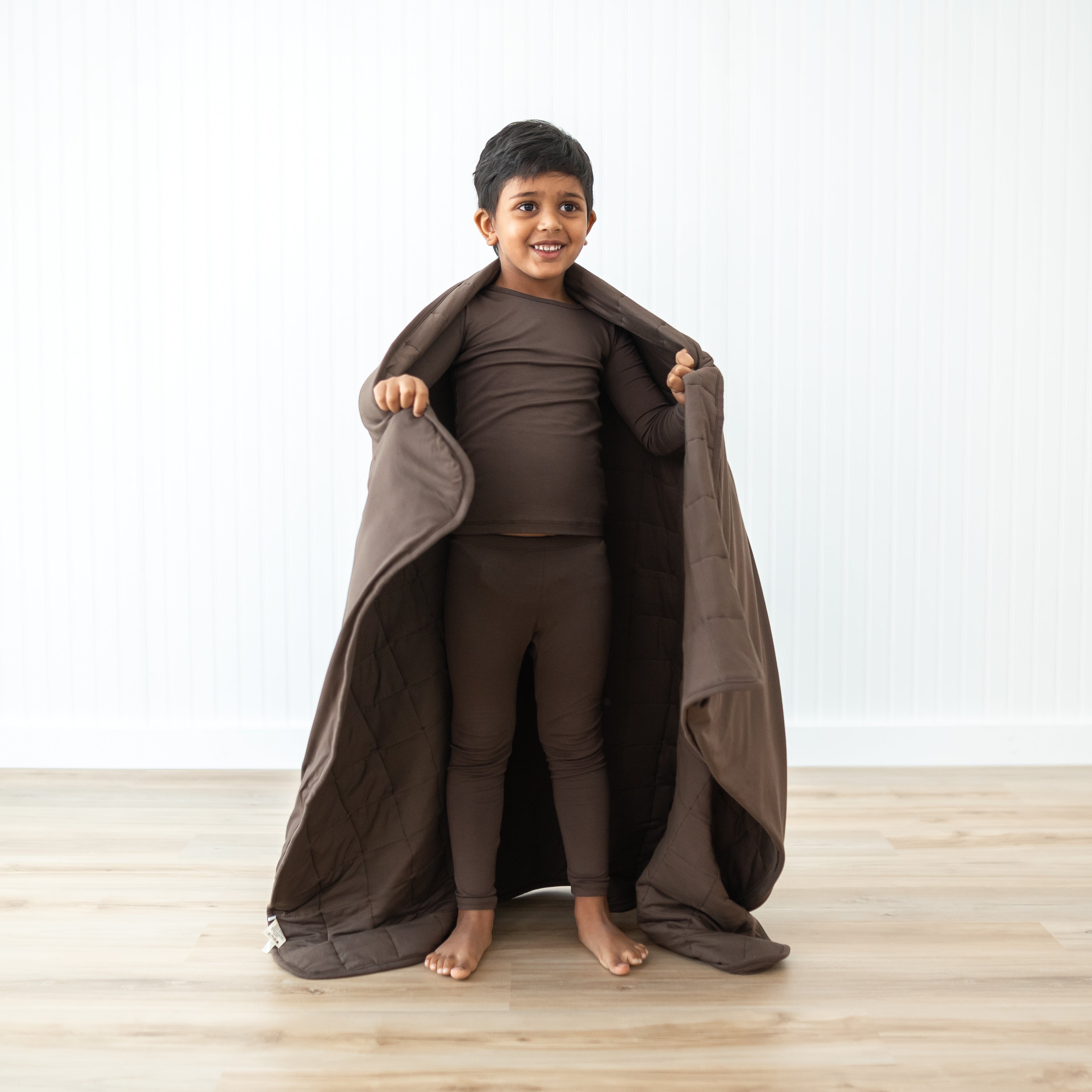 Boy model standing with the Toddler Blanket in Espresso 2.5 around him wearing matching toddler pajamas