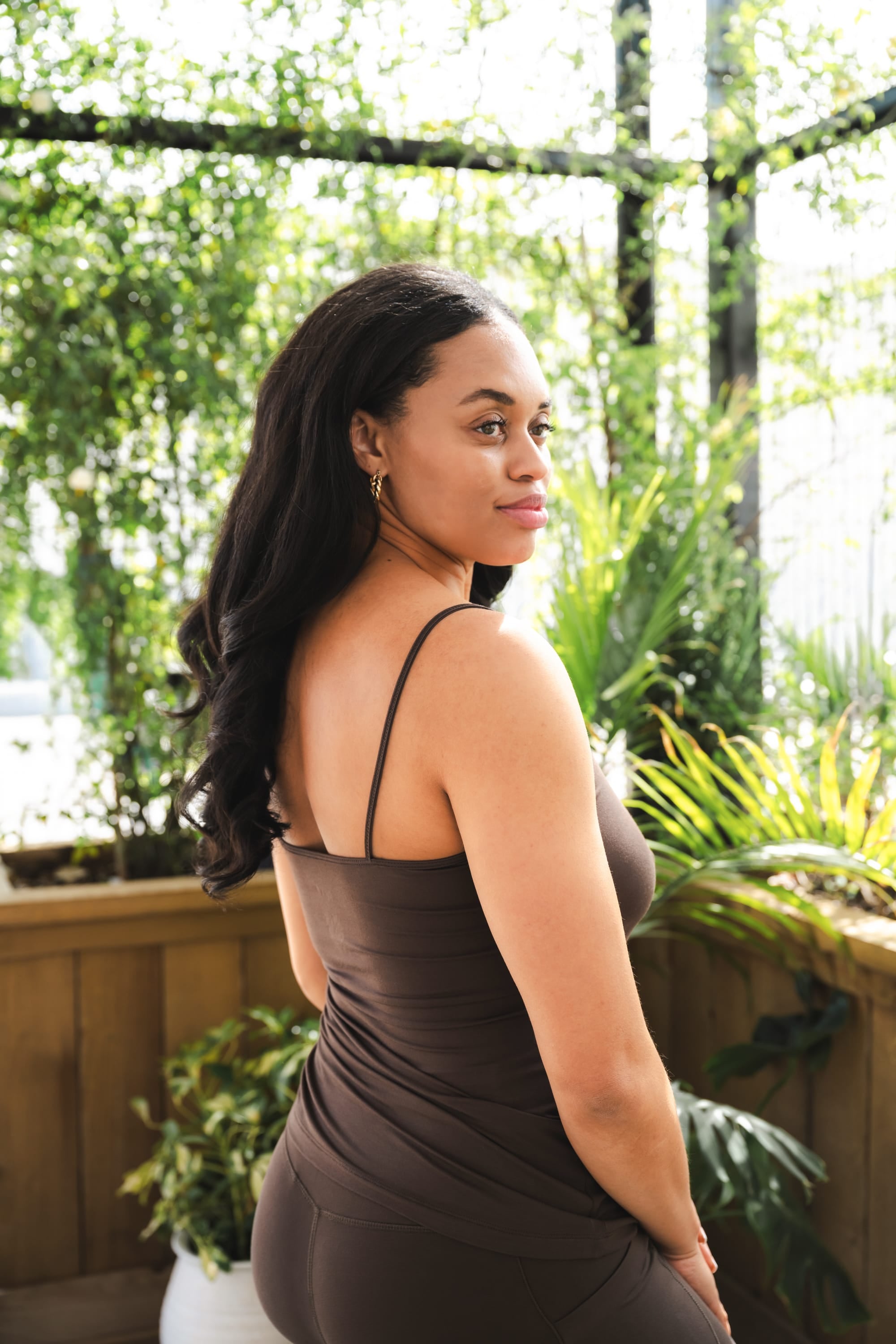Woman in a brown dress standing outdoors with greenery in the background