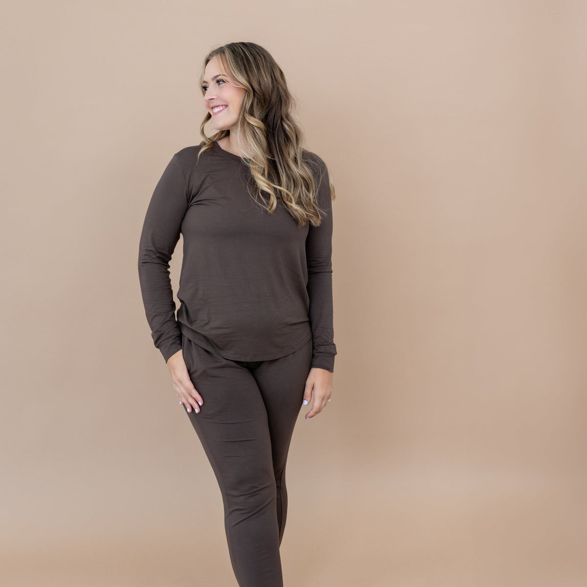Smiling female model with one hand in Women's Jogger Pajama Set in Espresso pants pocket looking off to the side
