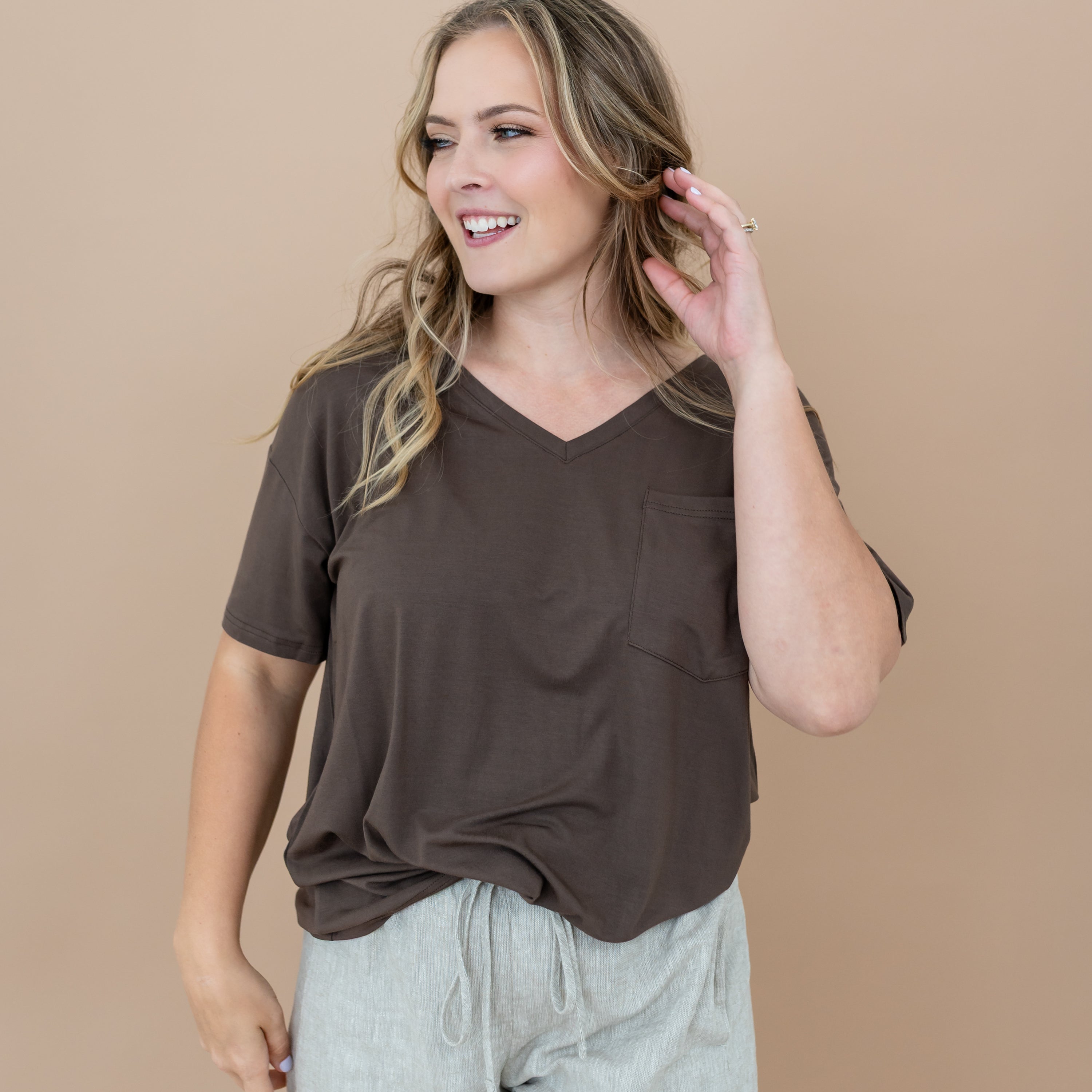 Female looking off to the side with her hand in her hair wearing the Women’s Relaxed Fit V-Neck in Espresso