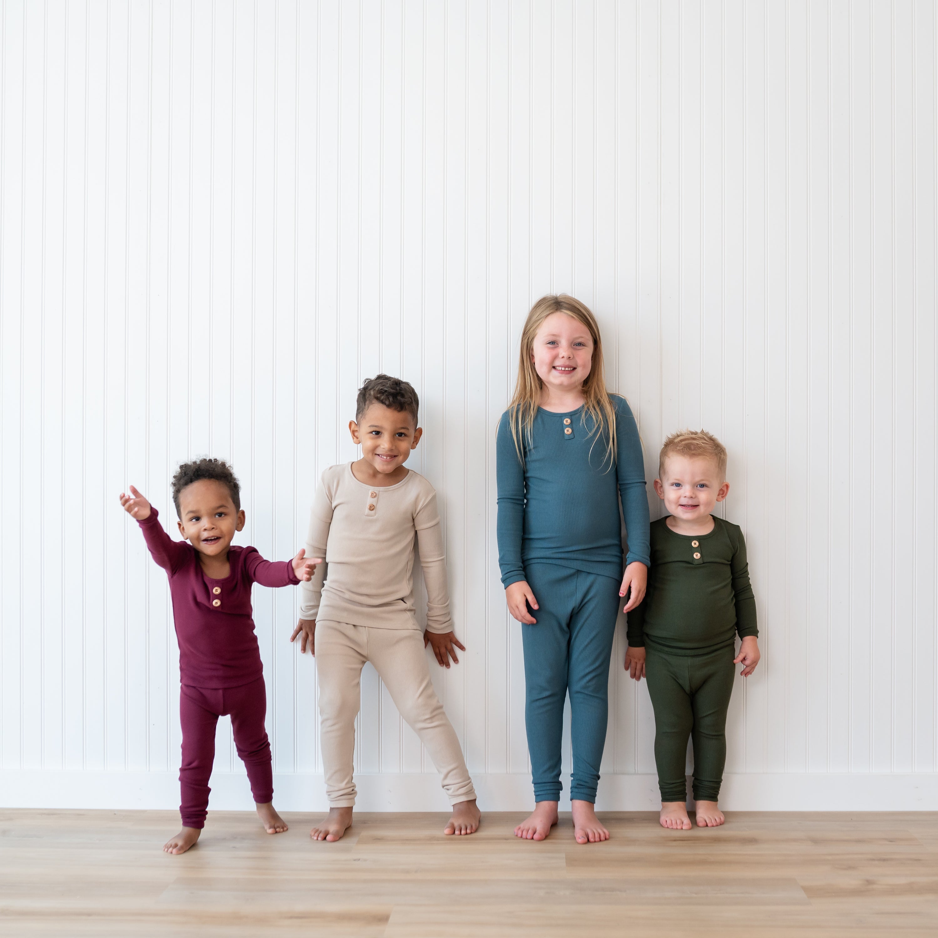 Four child models standing in front of a white wall all wearing the Ribbed Henley Set in Atlantic, Fir, Bisque and Burgundy
