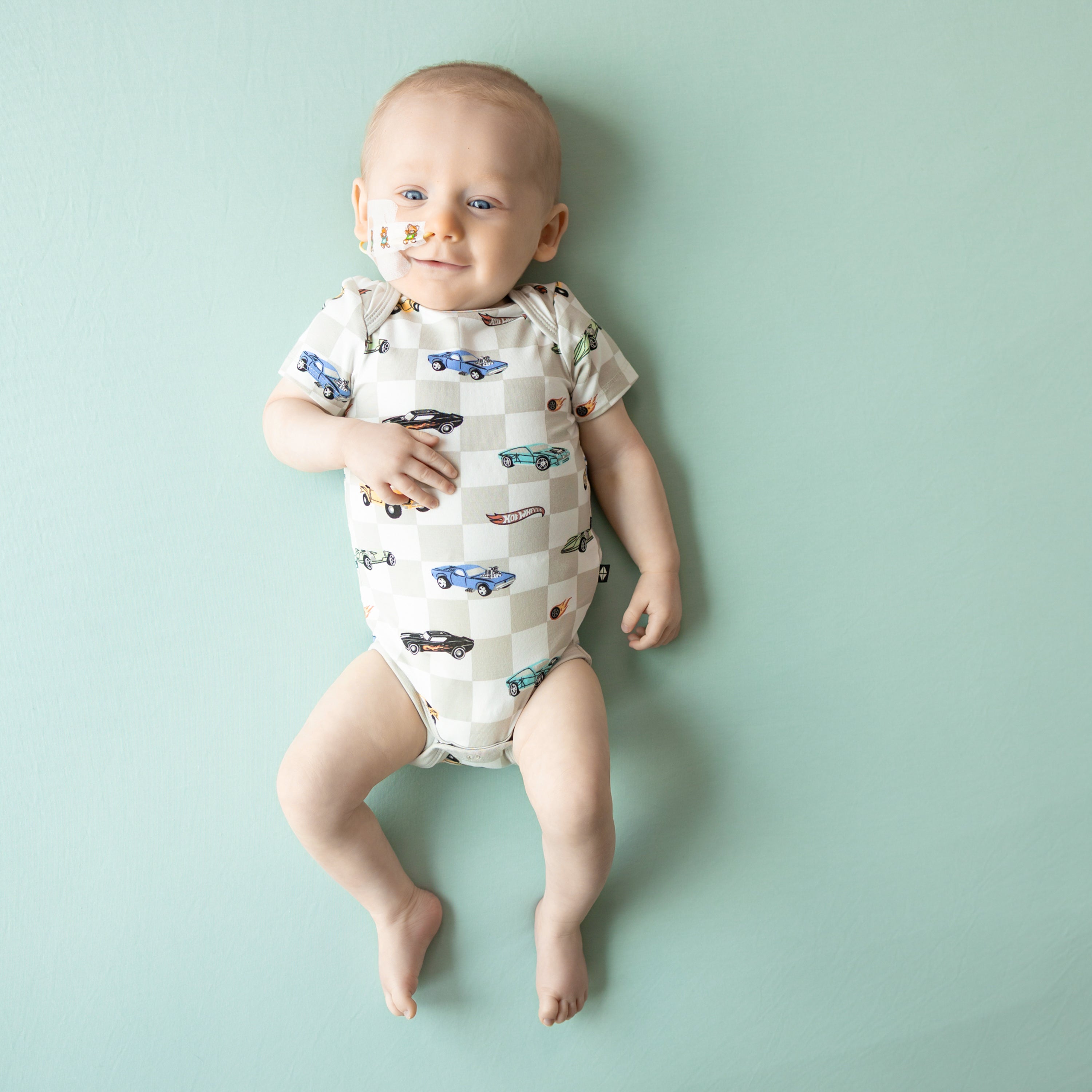 Smiling infant wearing the Bodysuit in Fast and Fierce laying on a Sage Blanket