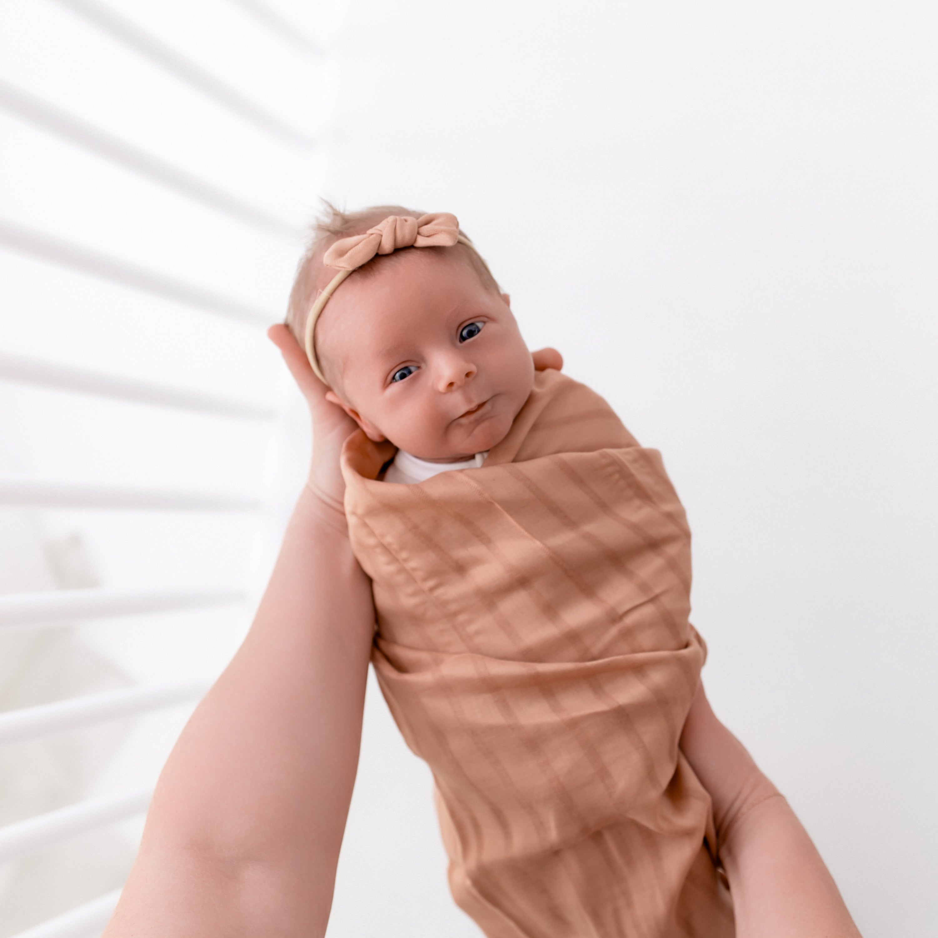 Baby swaddled in Bamboo Muslin Swaddle Blanket in Fawn Orange with matching bow