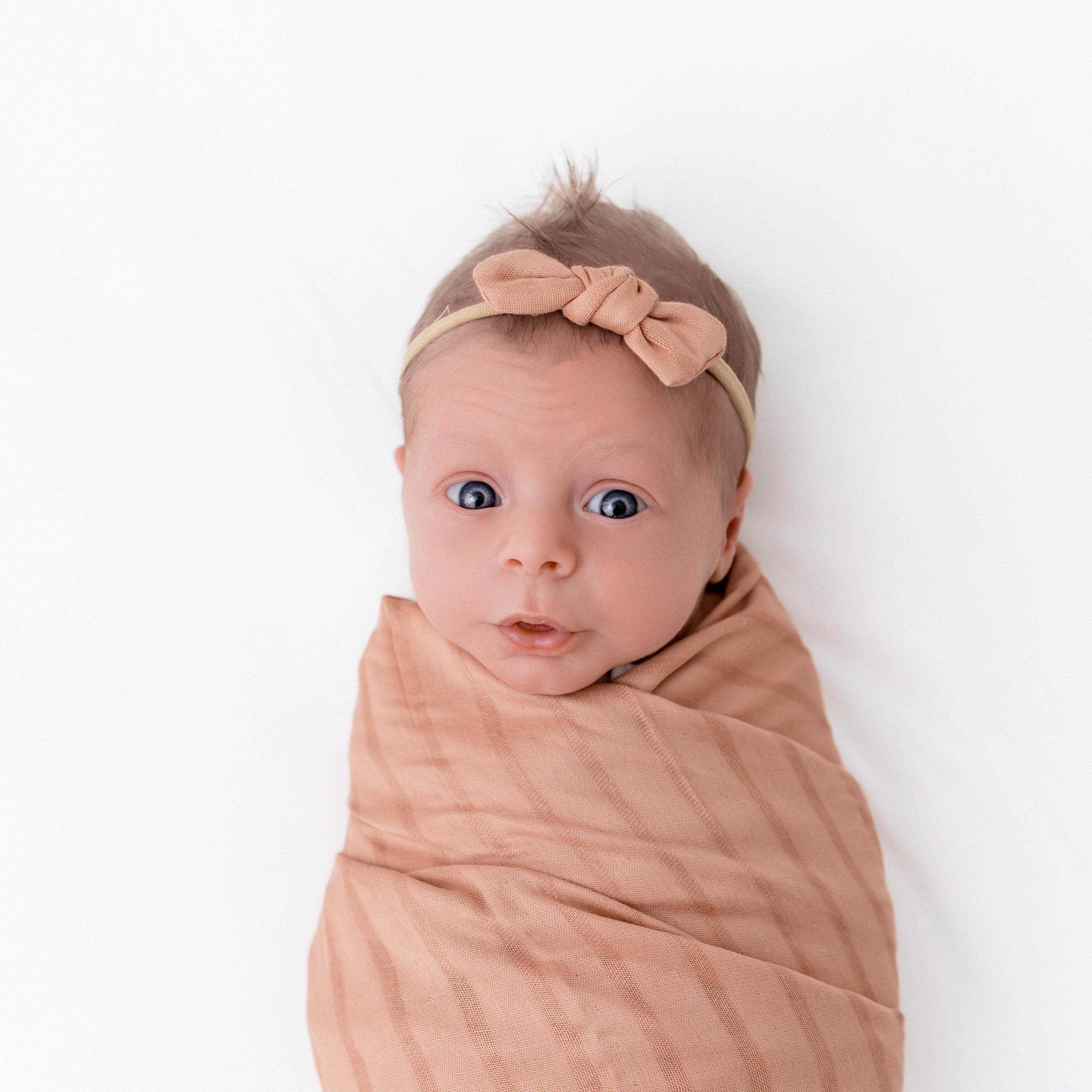 Baby wearing Bamboo Muslin Tiny Bow in Fawn wrapped in swaddle