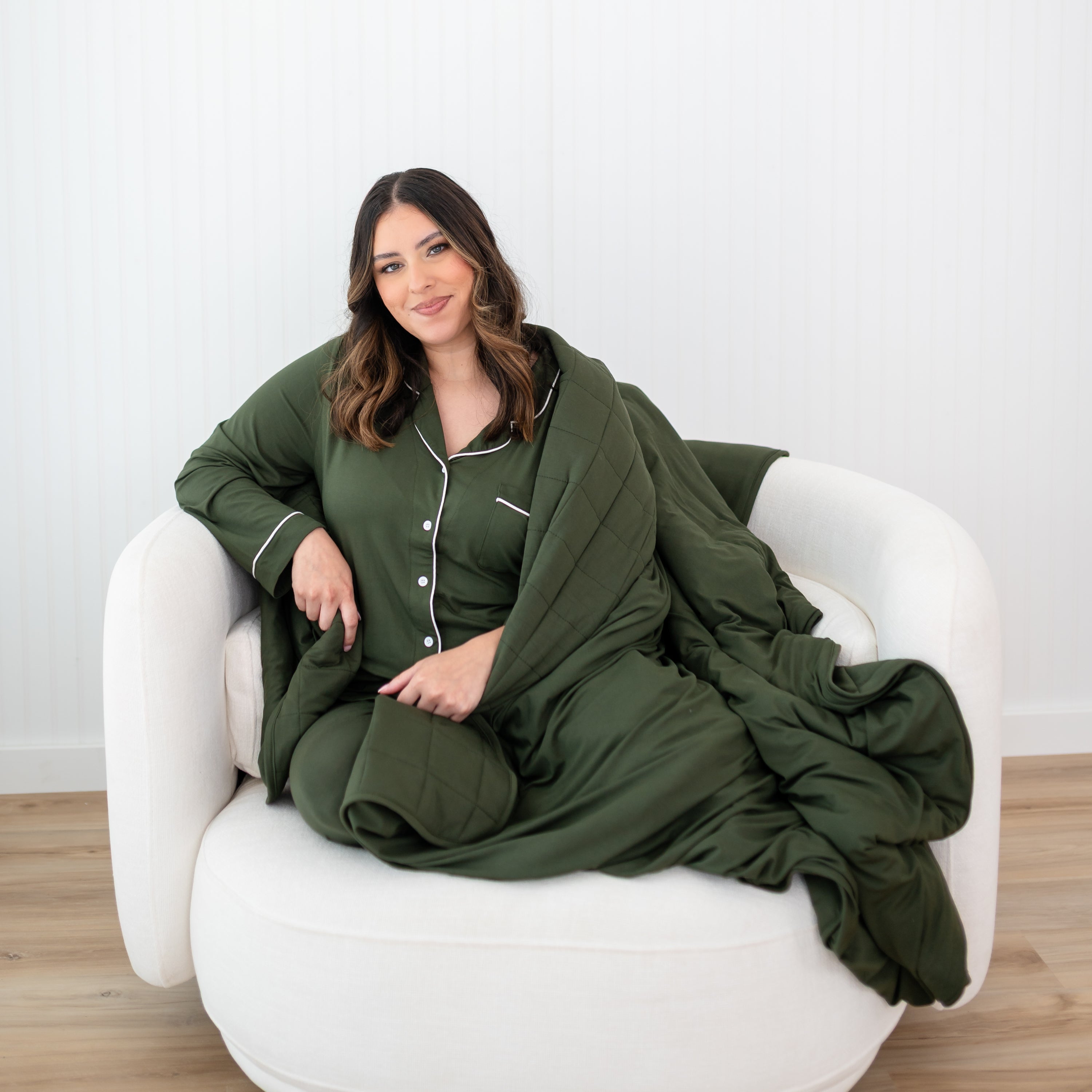 Woman in green pajamas sitting on a white chair with a green blanket draped over her.