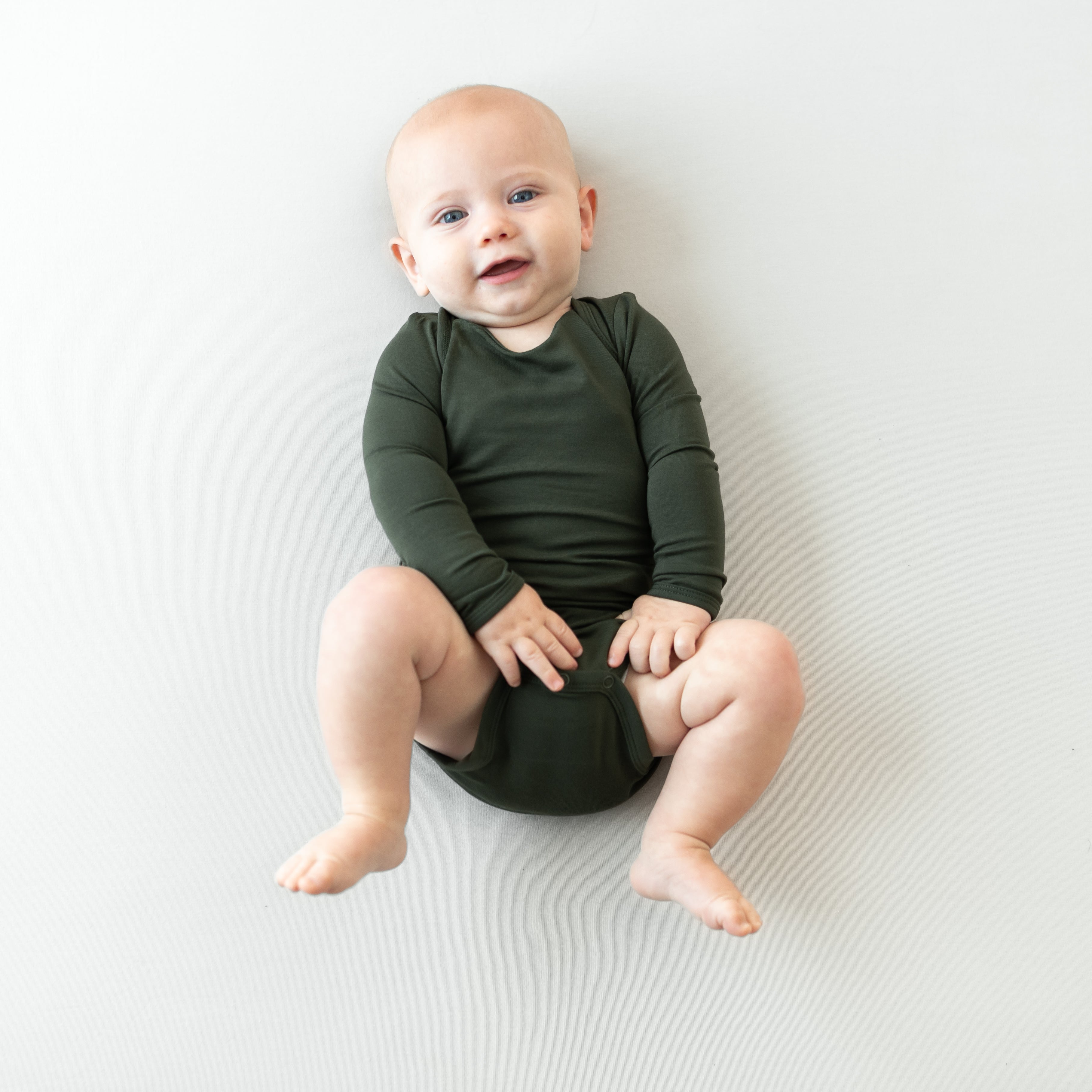 Baby in Long Sleeve Bodysuit in Fir laying on a neutral backdrop