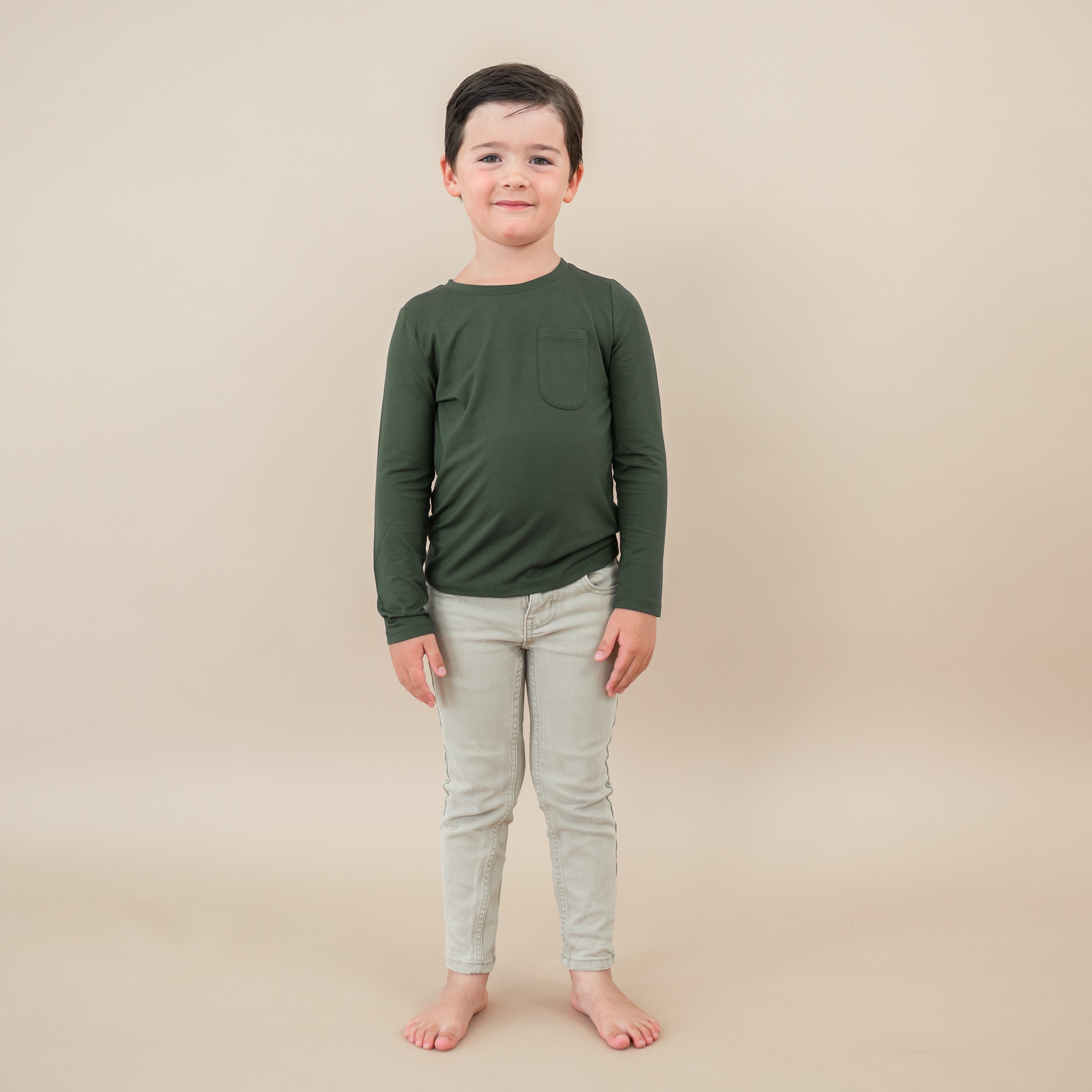 Toddler boy modeling Long Sleeve Toddler Crew Neck Tee in Fir on a tan backdrop