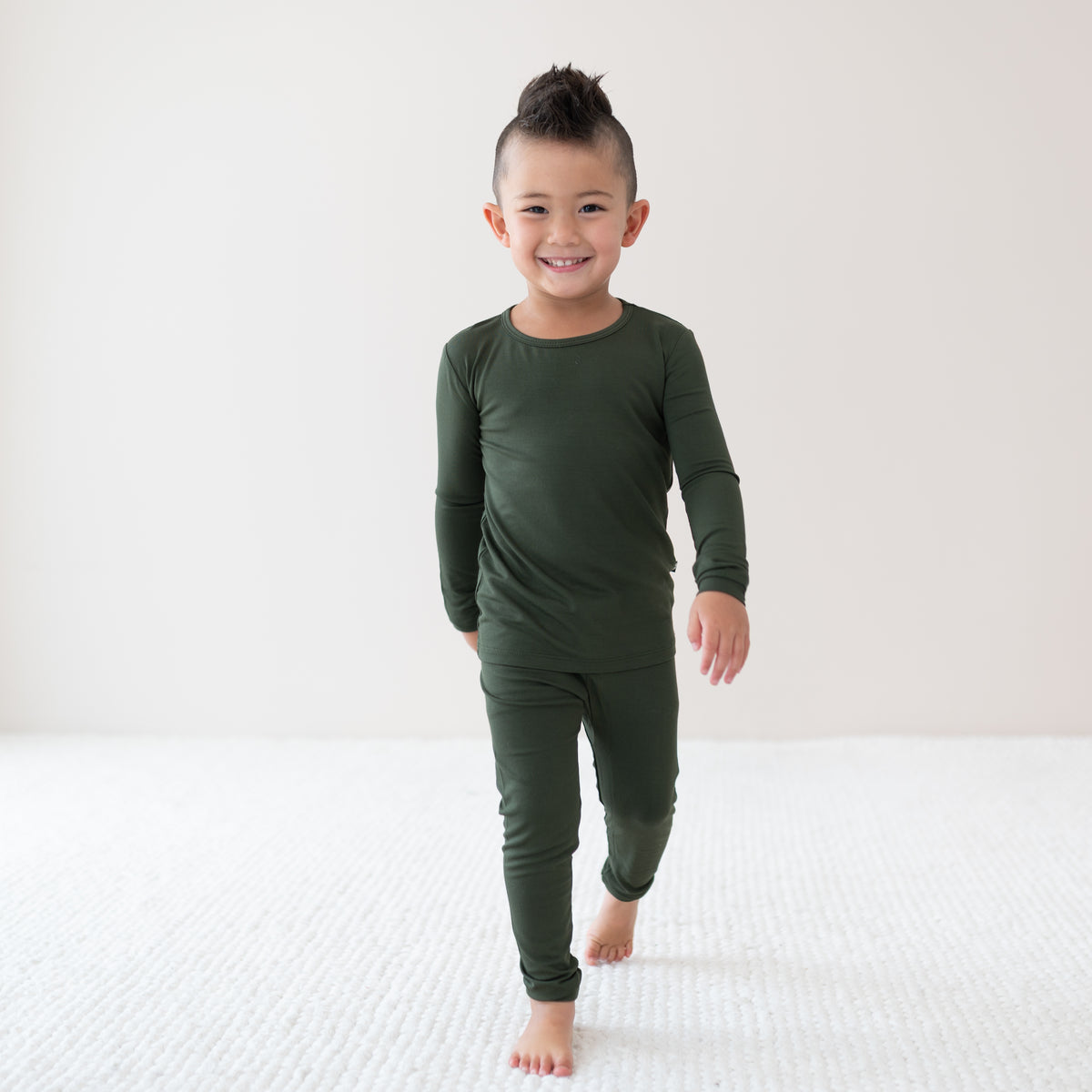 Toddler wearing Long Sleeve Pajamas in Fir on a neutral backdrop and cream rug